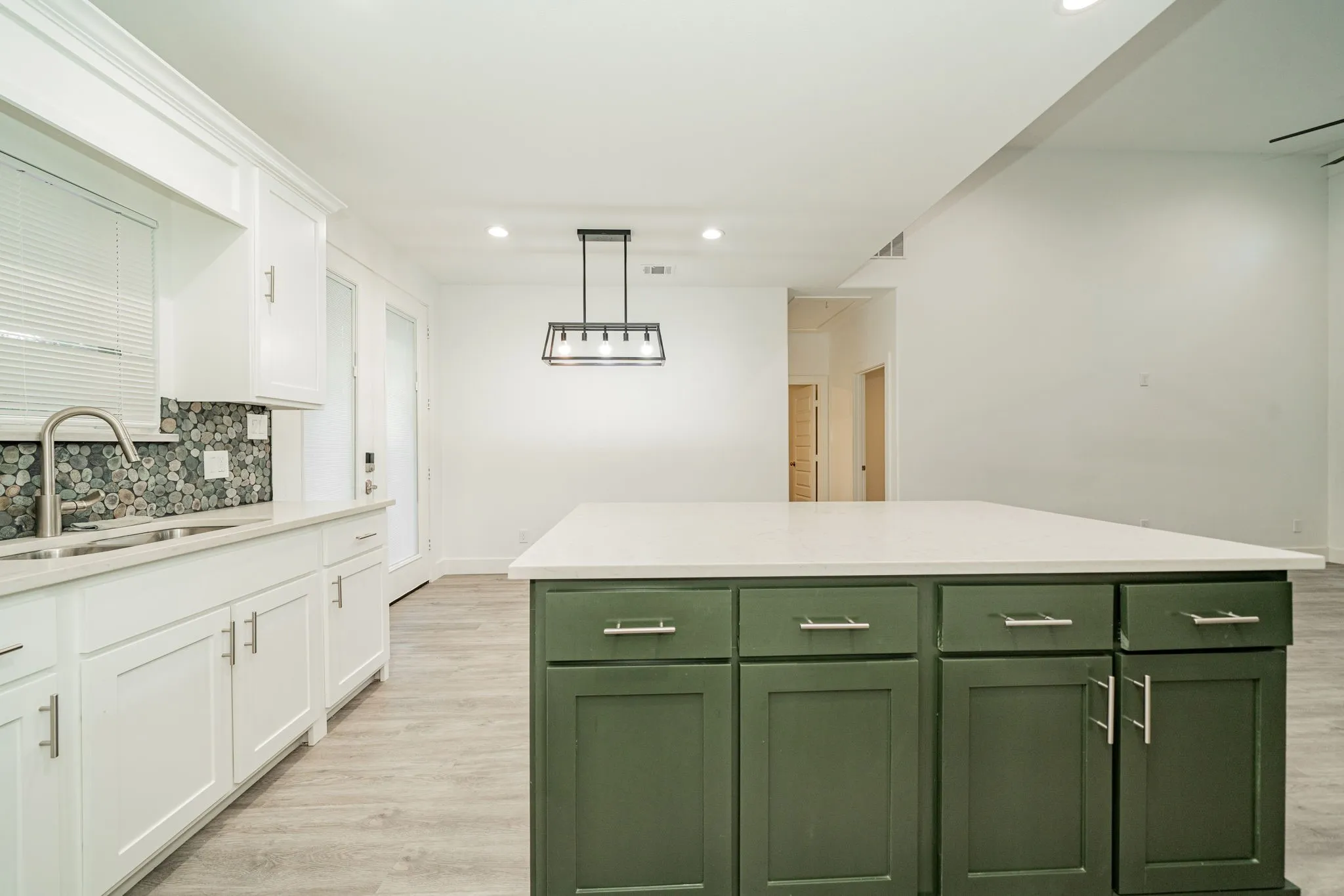 Kitchen featuring white cabinetry, a natural stone mosaic tile backsplash, a center island with green cabinetry and a solid surface countertop, and wood-finish flooring