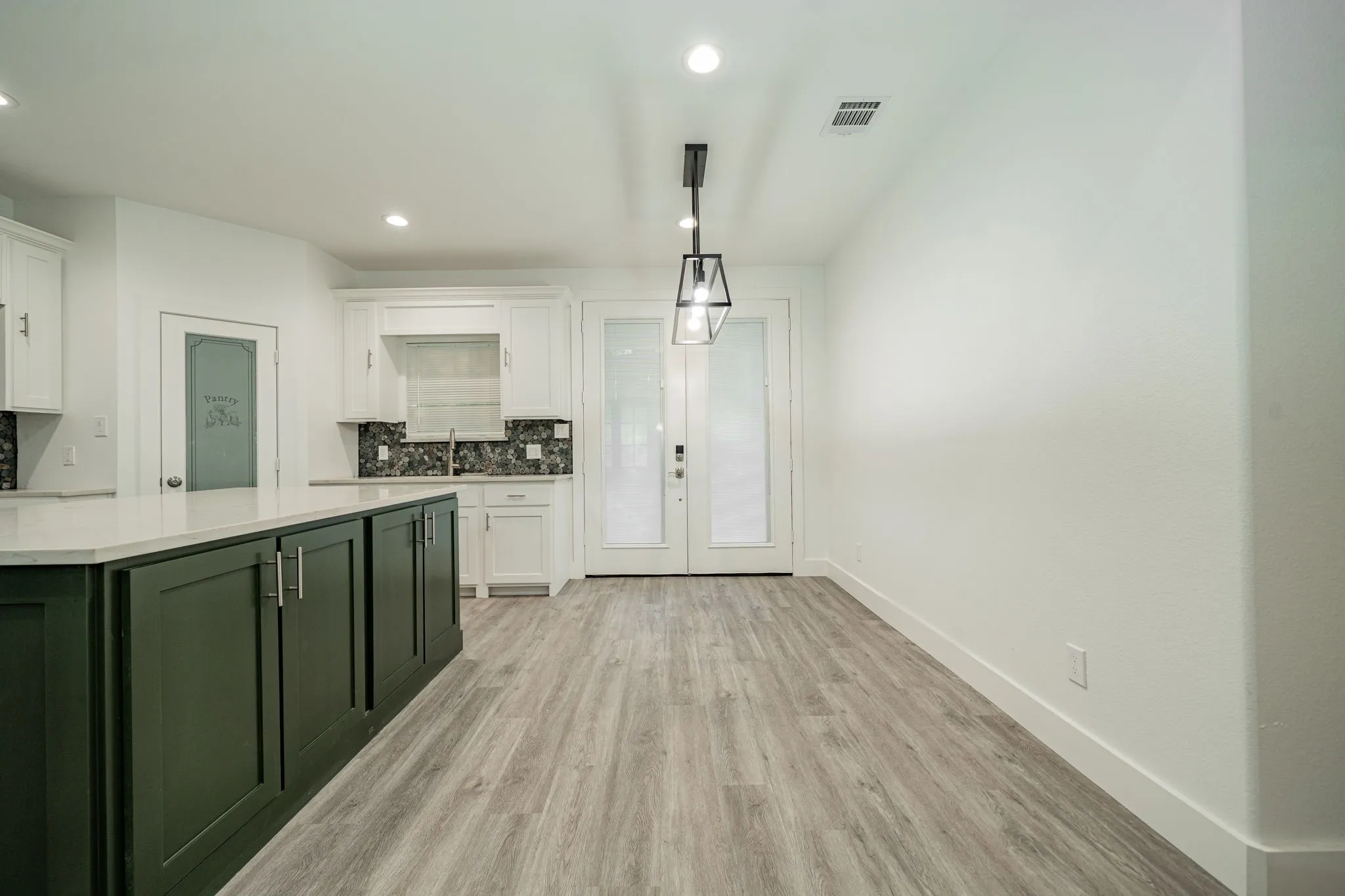 Kitchen featuring a large island with dark green cabinetry, white countertops, wood-finish flooring, a mosaic tile backsplash, and recessed lighting