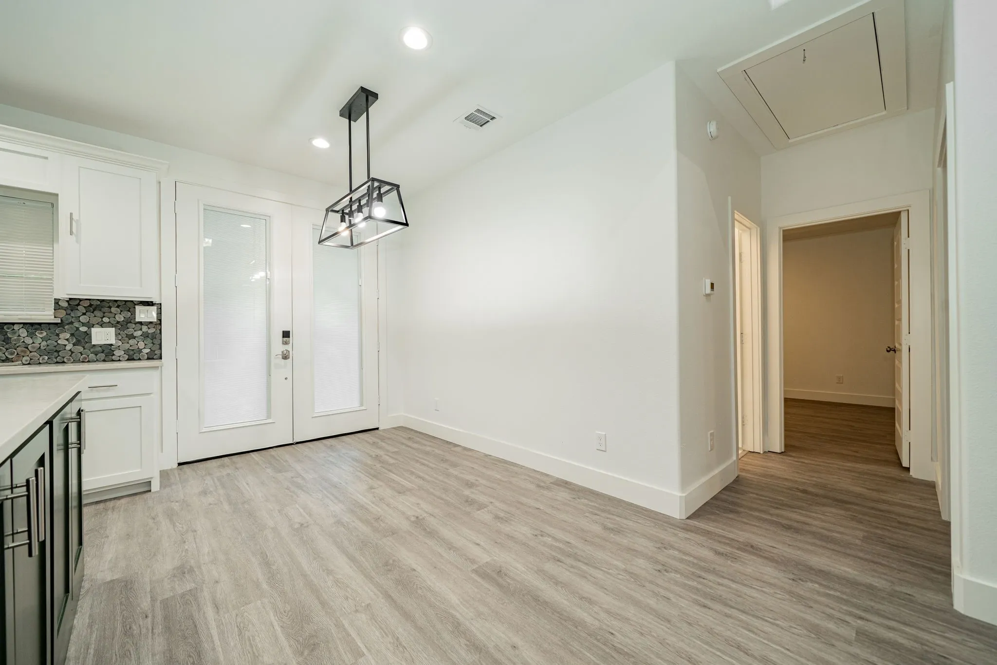 Wood-finish flooring, white cabinetry, decorative tile backsplash, recessed lighting, and a modern chandelier