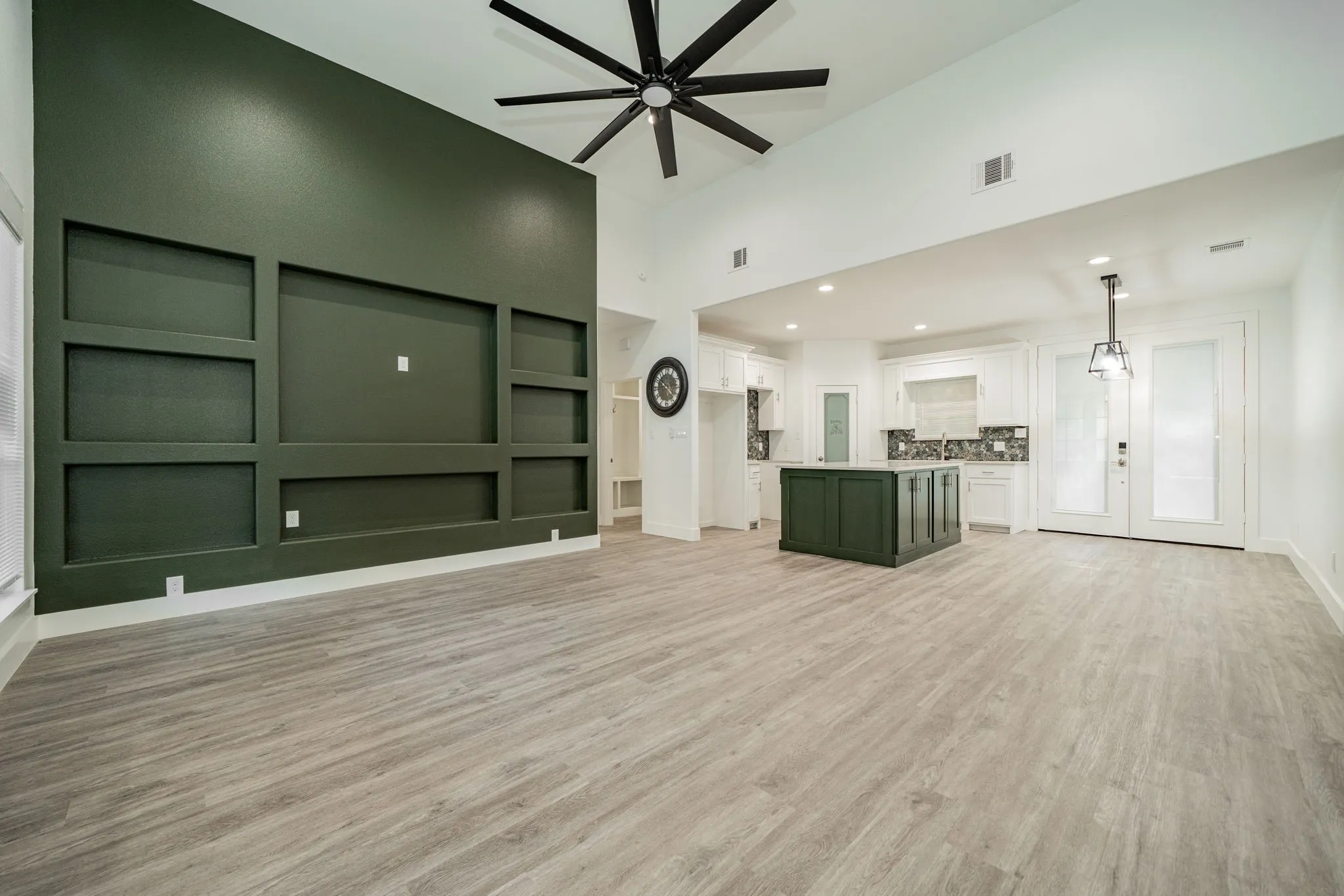Vaulted ceilings with a ceiling fan, accent wall with built-in shelving, wood-finish flooring, kitchen island with cabinet storage, and recessed lighting