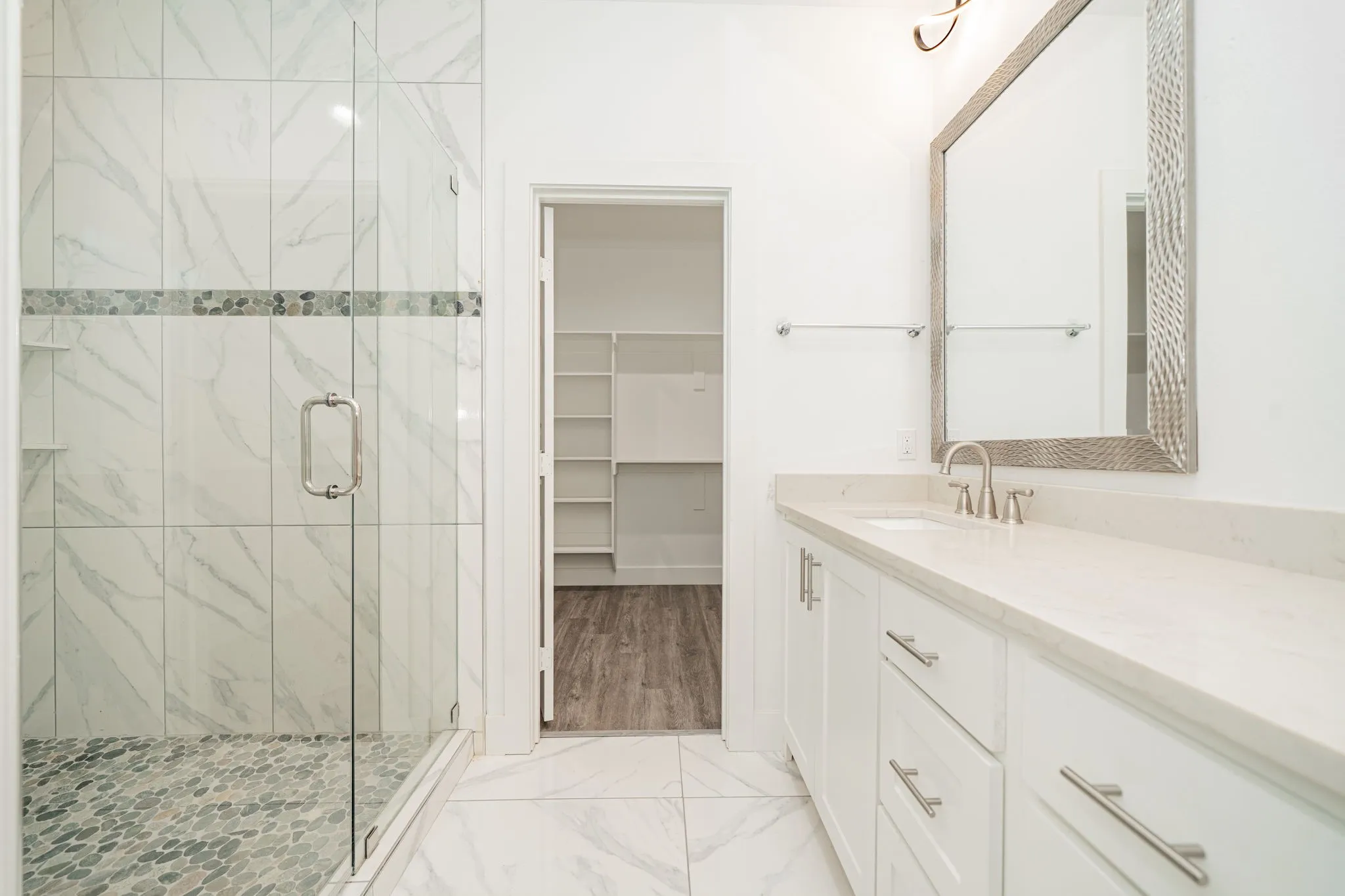 Glass-enclosed shower with a pebble tile floor and a decorative tile band