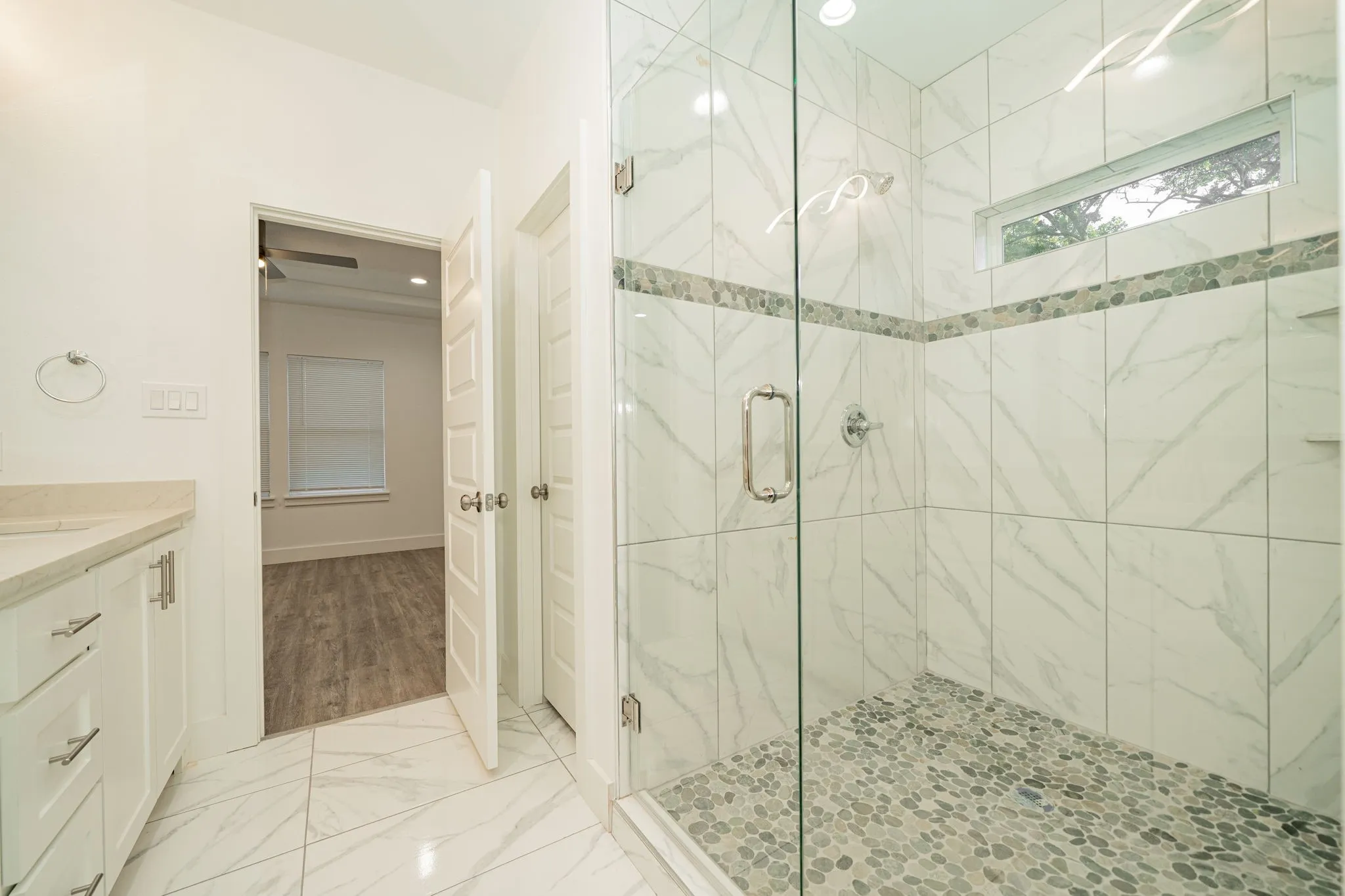 Glass-enclosed shower with a pebble floor and marble-look tile walls