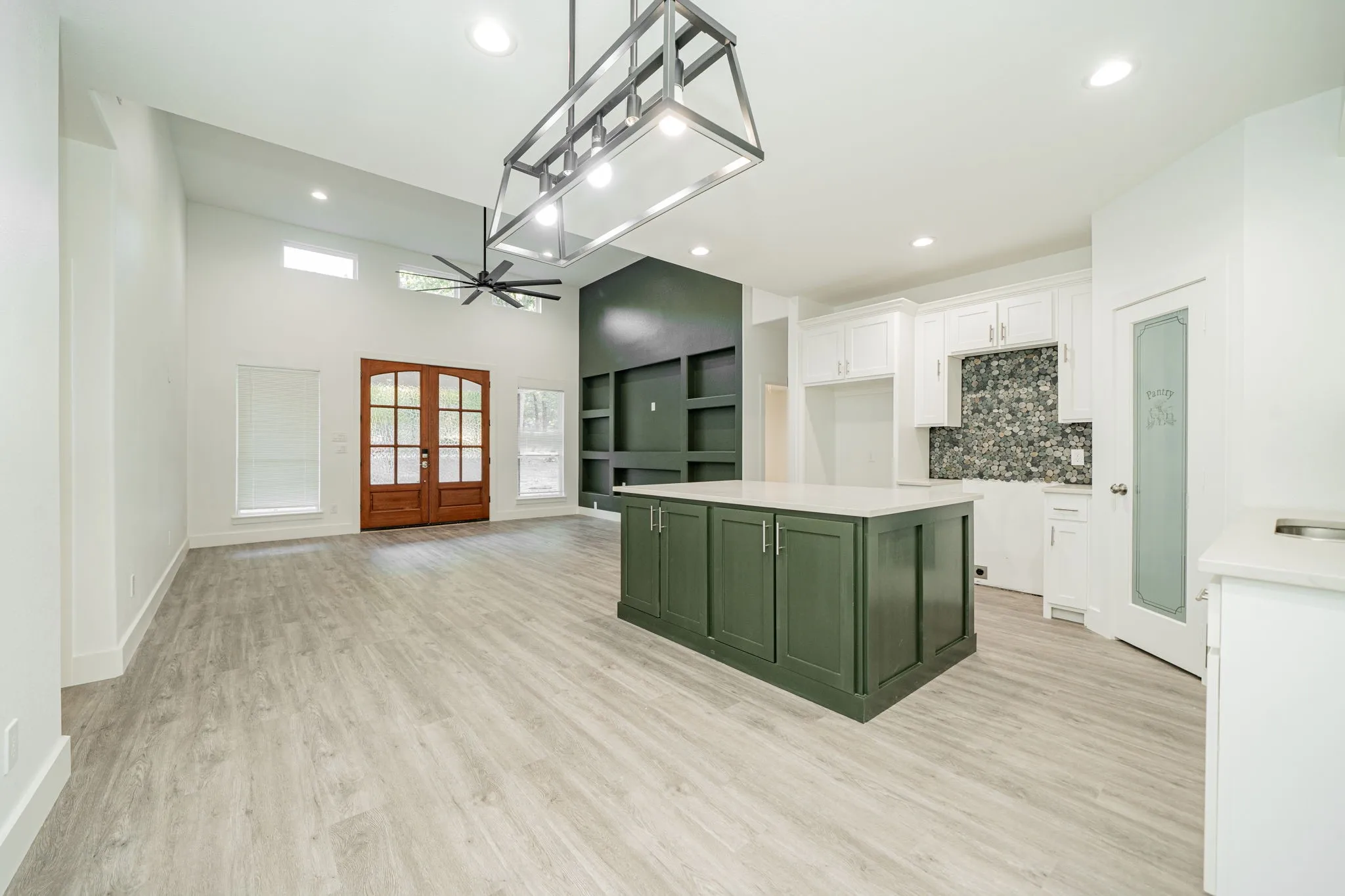 Vaulted ceiling with a contemporary chandelier, light wood-finish flooring, and a kitchen island with built-in storage