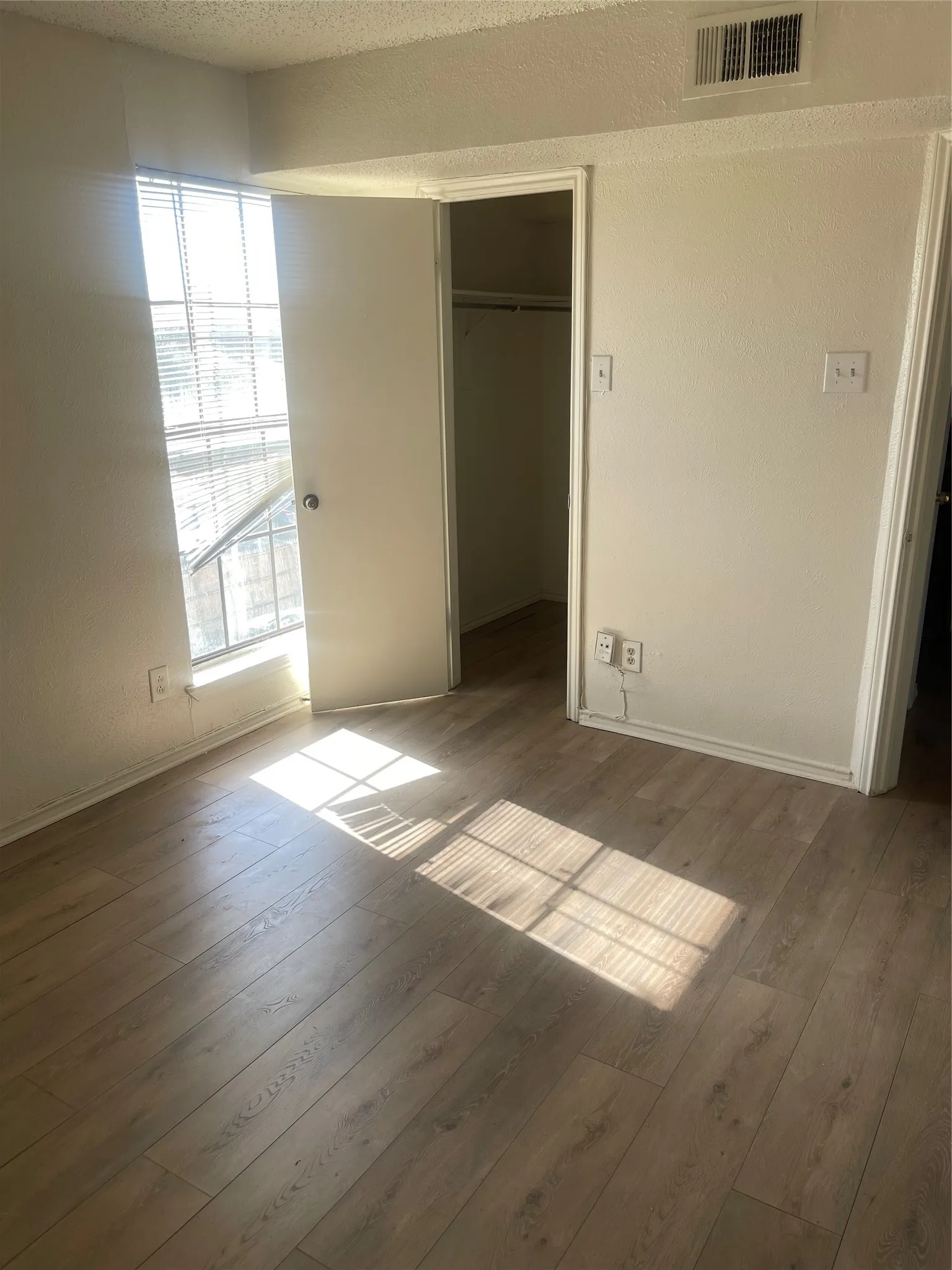 Wood-finish flooring throughout, bright window with horizontal blinds, and a built-in closet