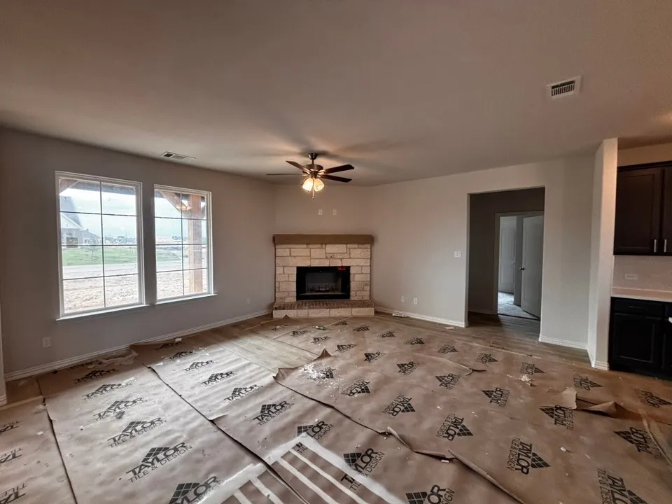 Spacious living area featuring a stone-clad fireplace with a wood mantel, two large windows, a ceiling fan, and recessed lighting