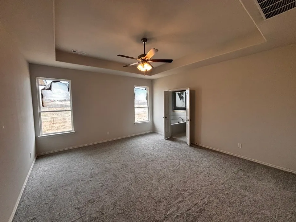 Spacious room featuring a tray ceiling with a built-in ceiling fan, light gray carpeting, and two double-hung windows