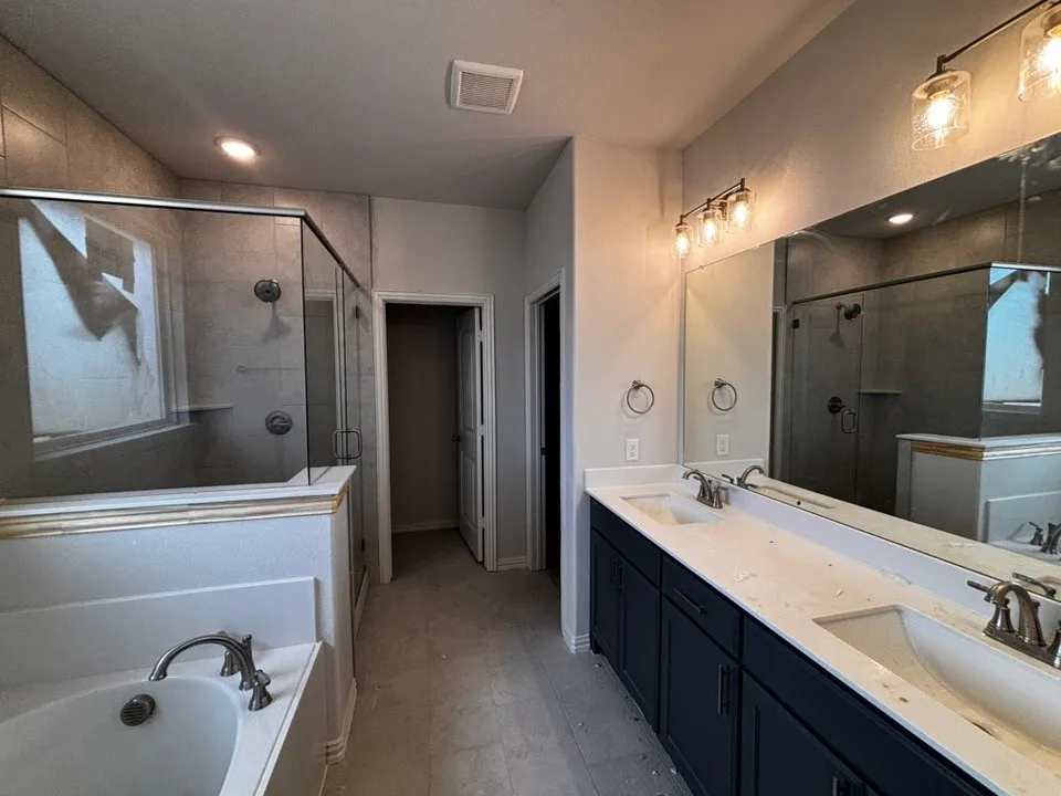 Dual vanity with undermount sinks, frameless shower enclosure, separate soaking tub, tiled shower surround, and recessed lighting