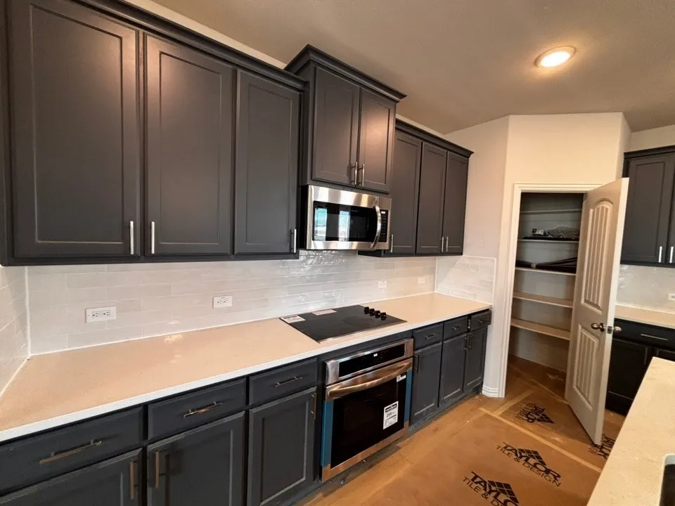 Dark cabinetry with stainless steel hardware, built-in stainless steel microwave, integrated cooktop, stainless steel oven, and light-toned countertops