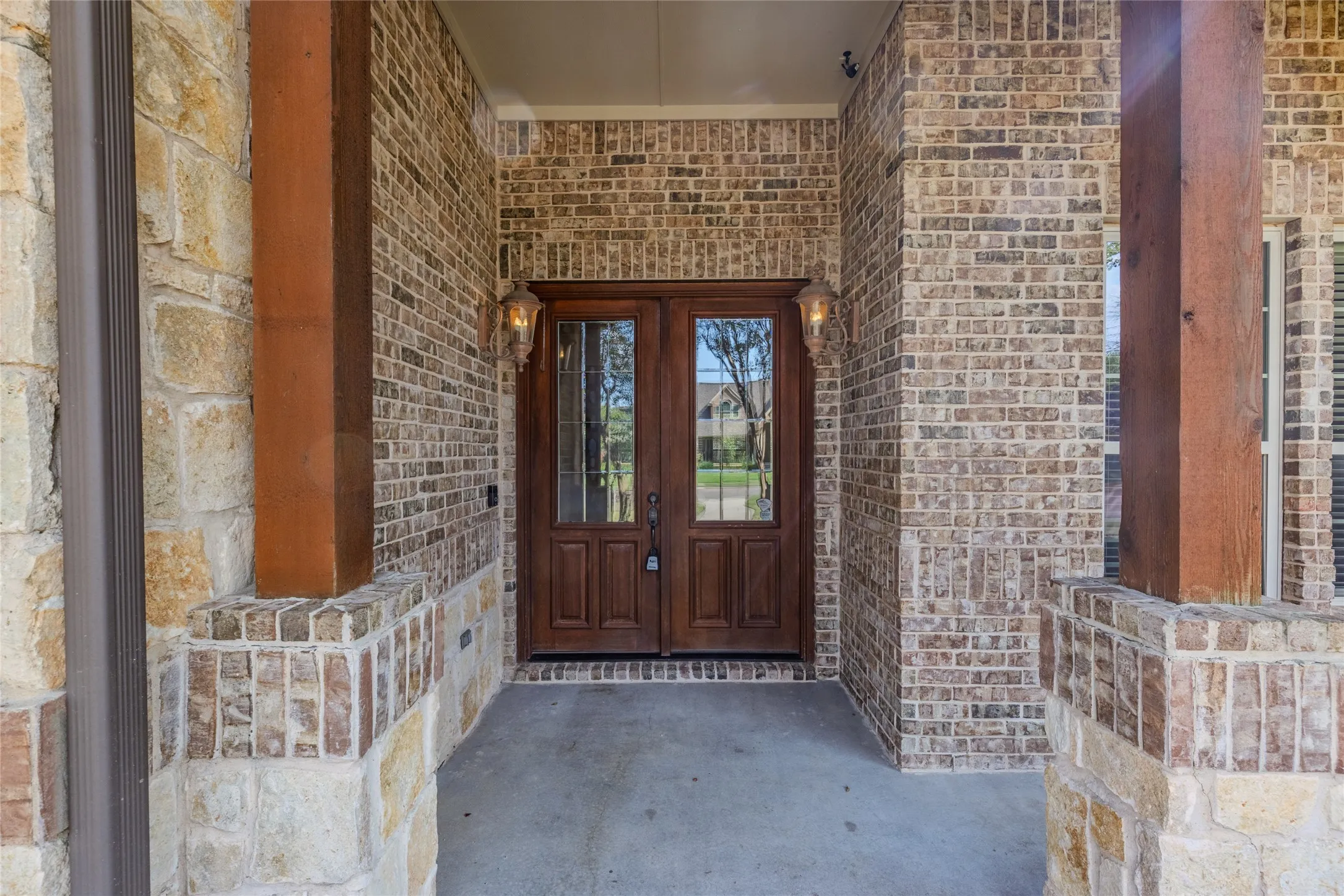 Inviting entry with double wood doors, brick facade, stone accents, and decorative outdoor lighting