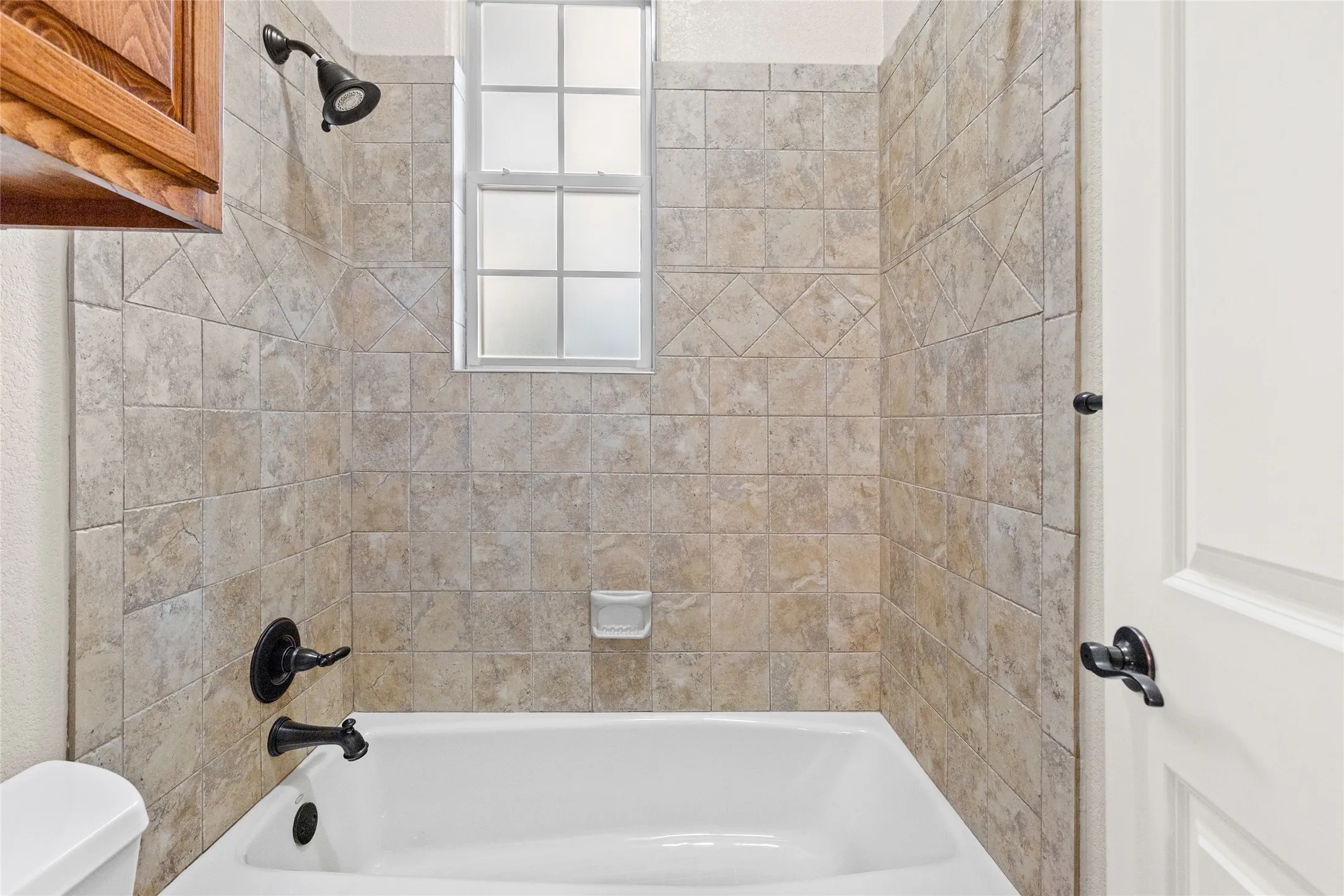Bathtub with tile surround, black-finish fixtures, and a frosted window