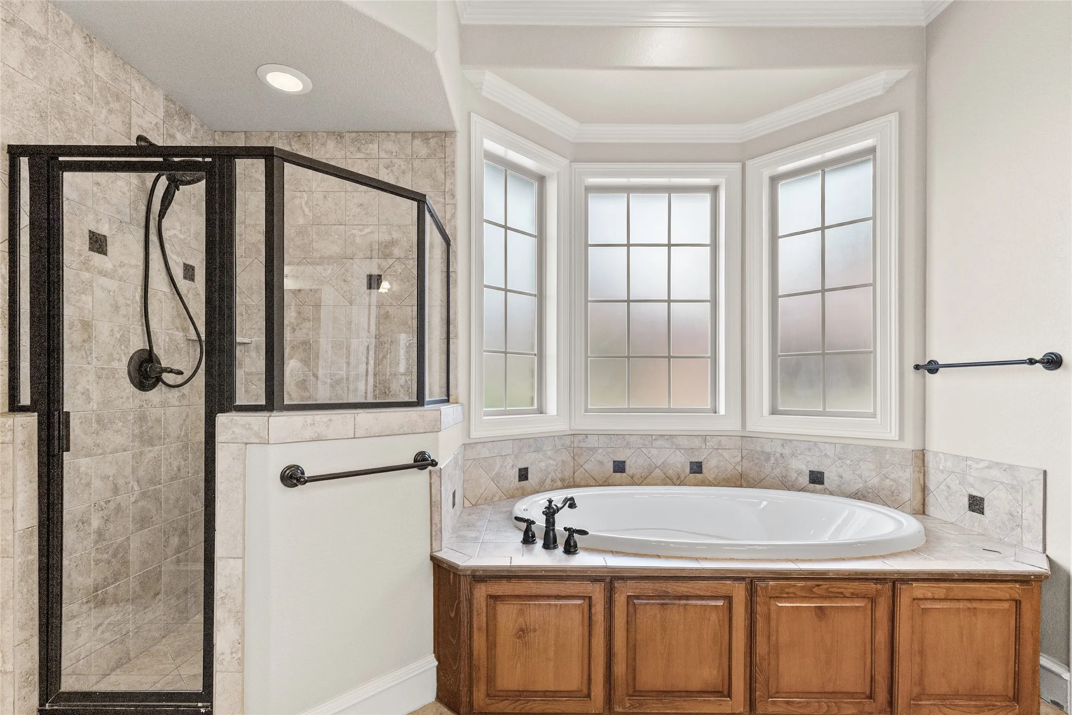 Built-in bathtub with corner bay windows, wood-finish cabinetry, and an enclosed shower with dark-framed glass