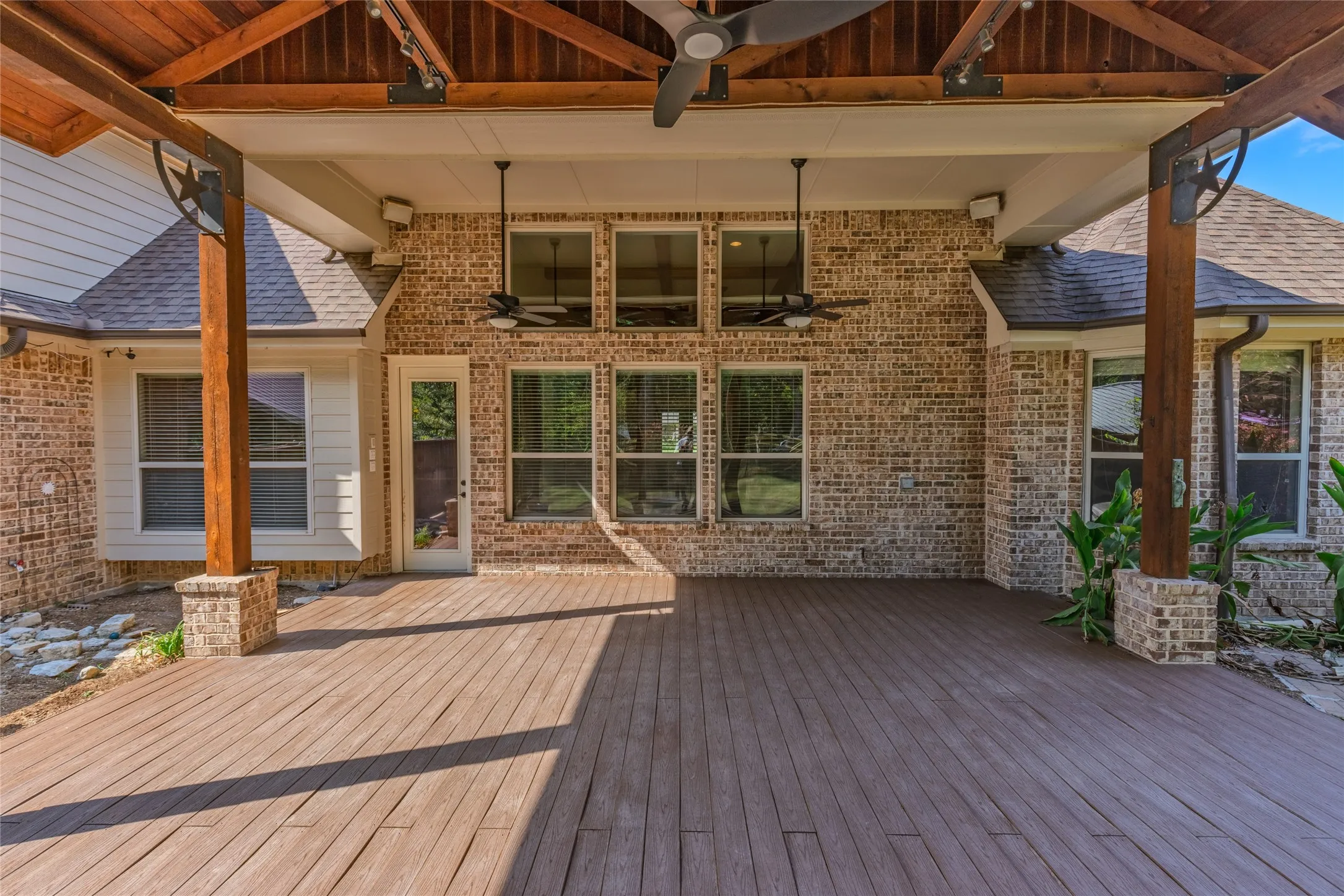 Expansive covered patio featuring a wood-finish deck, brick exterior, and multiple ceiling fans