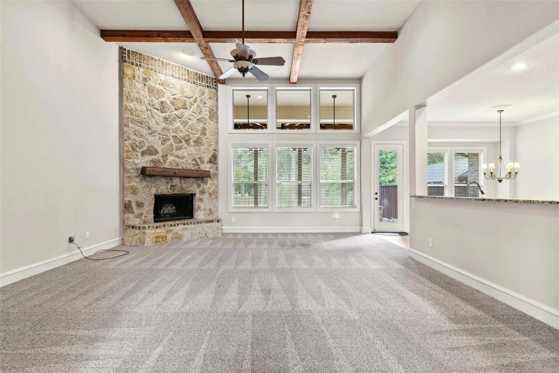 Vaulted ceilings with exposed wood beams, stone fireplace with a wood mantel, multi-pane windows, and a built-in breakfast bar with a granite countertop