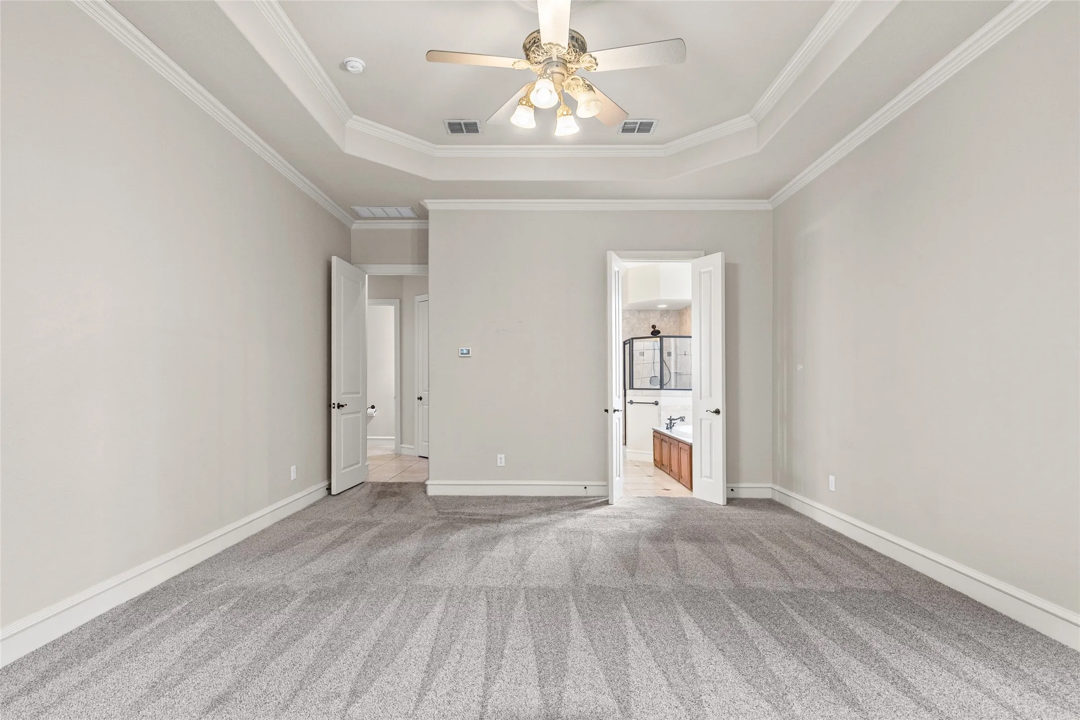 Recessed ceiling with crown molding, ceiling fan, and light-toned carpet flooring