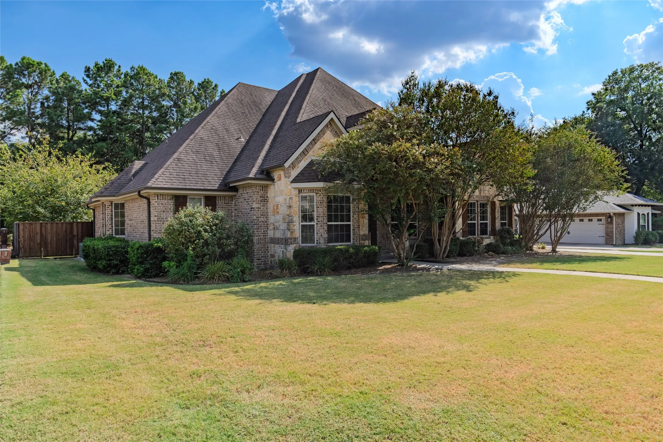 Brick and stone exterior, multi-gabled roofline, mature landscaping, integrated two-car garage, and a fenced side yard