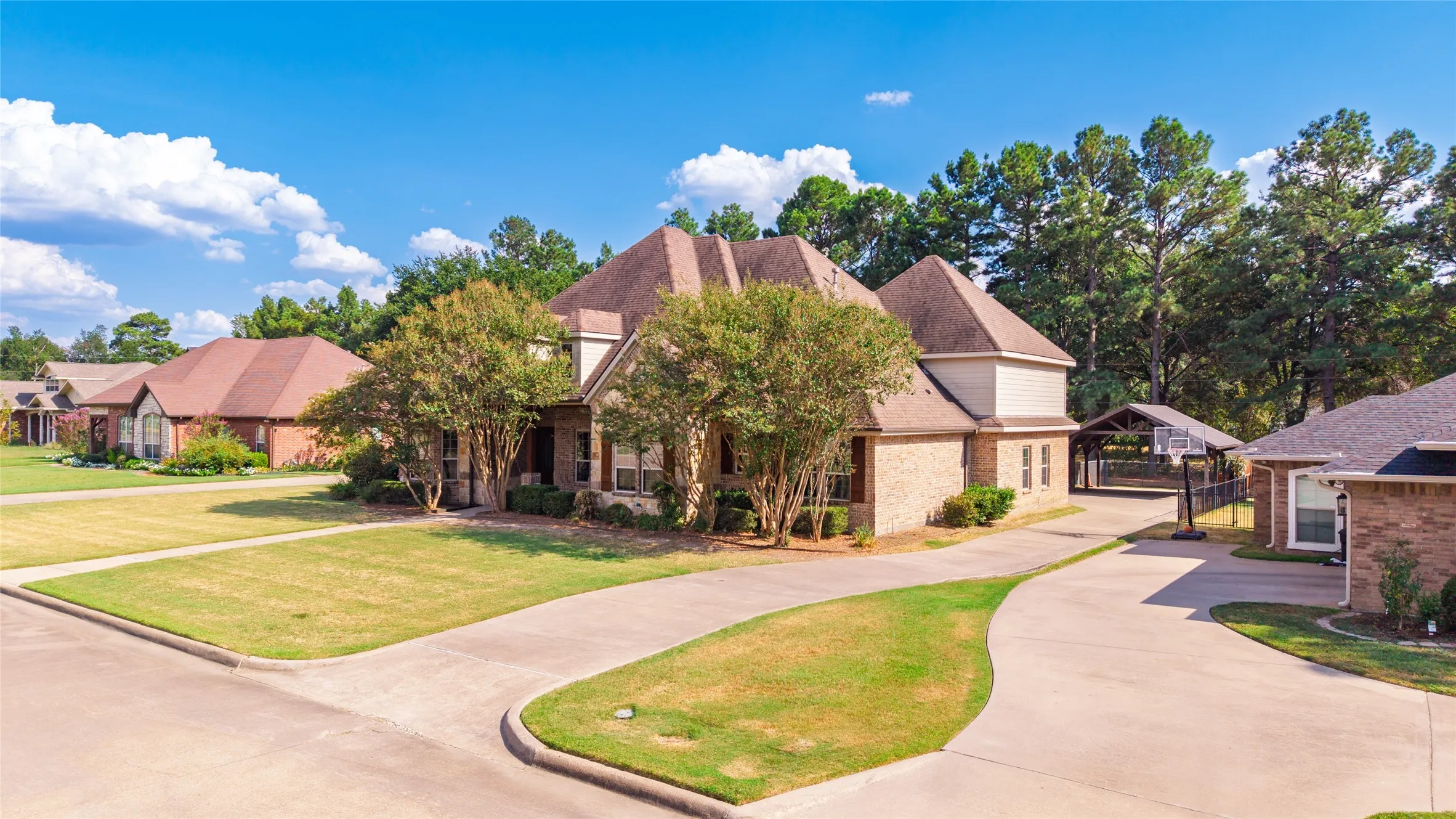 Brick exterior residence with a multi-level roofline, extensive paved driveway, and mature landscaping