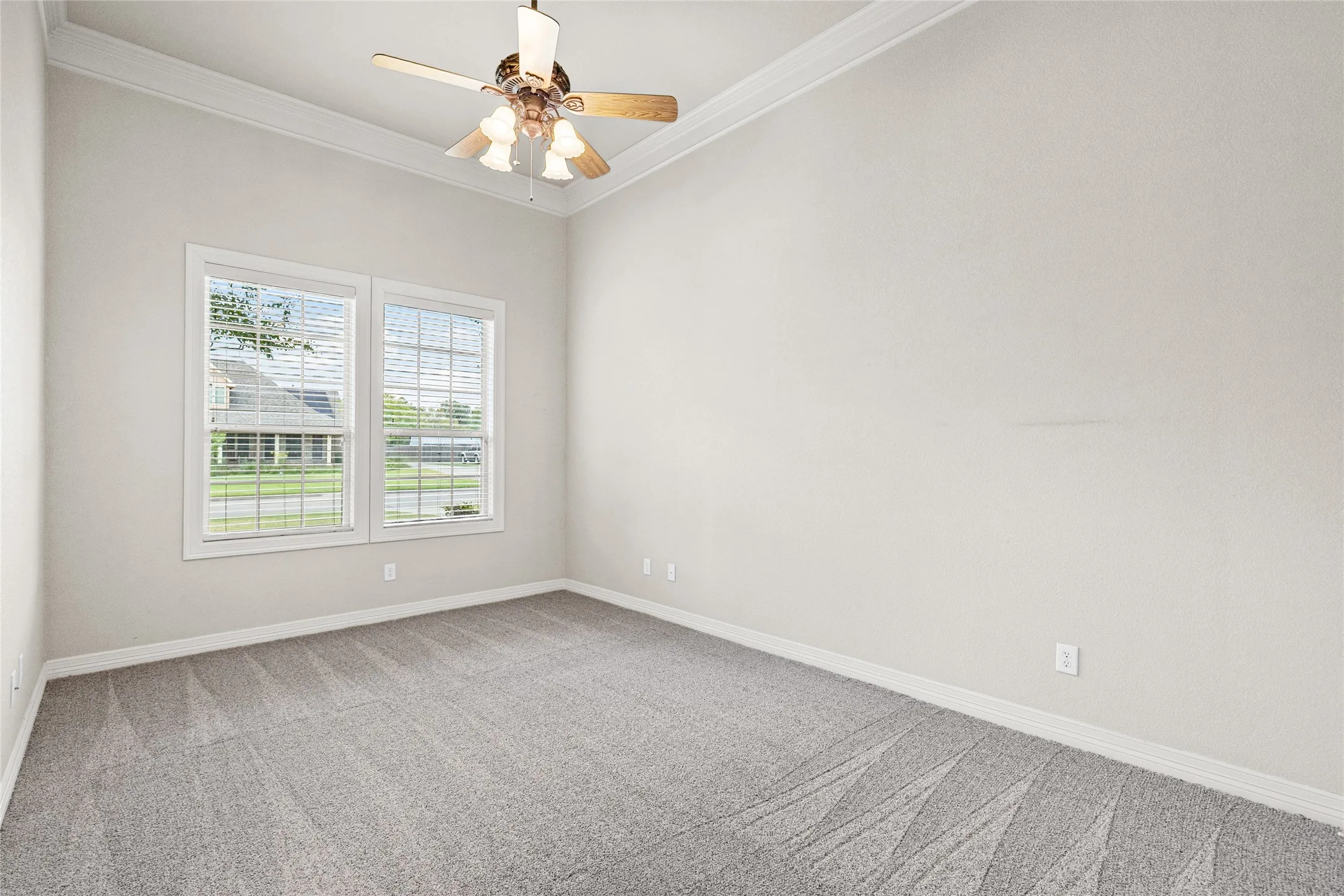 Vaulted ceiling with crown molding, two large windows, ceiling fan with light fixture, and plush carpeting