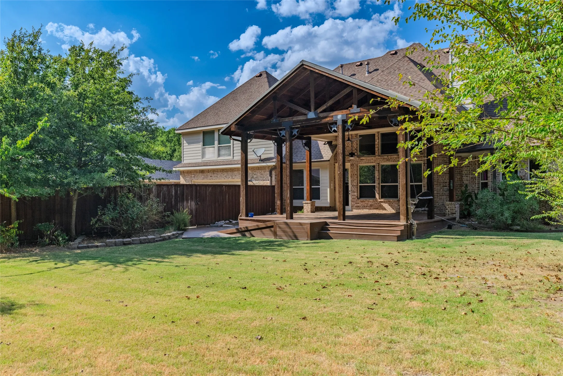 Expansive backyard featuring a covered patio with exposed wood beams, a multi-level wood deck, and a privacy fence