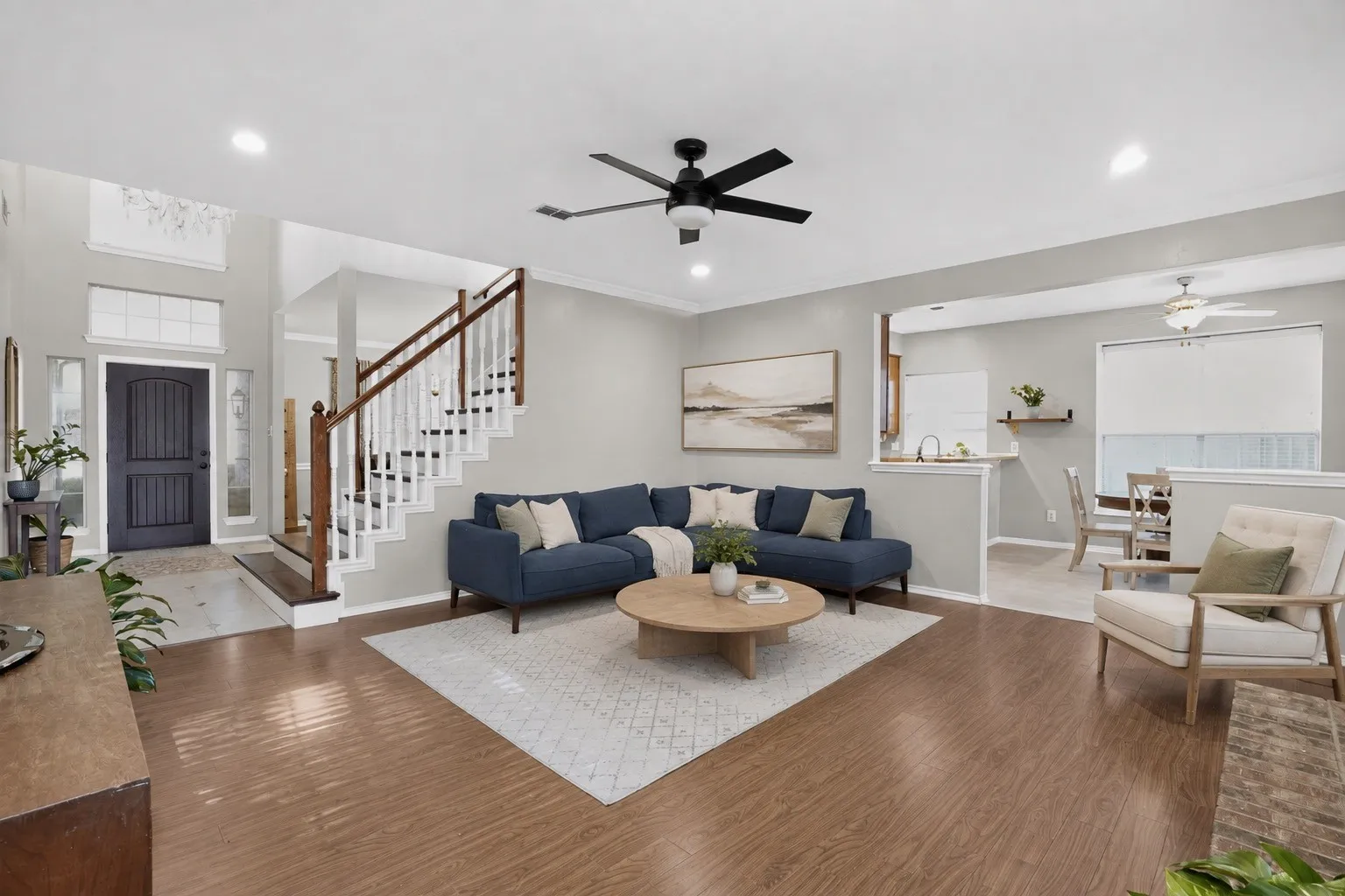 Wood-finish flooring throughout, vaulted entryway with transom window, staircase featuring wood handrails and white balusters, recessed lighting, and a ceiling fan with light fixture