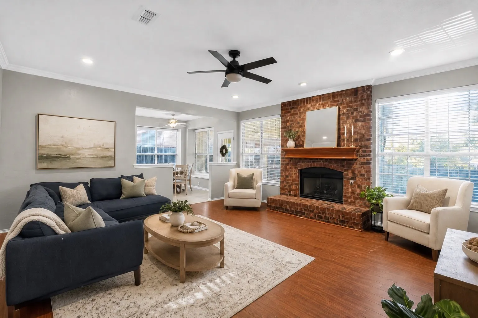 Spacious living area featuring wood flooring, a brick fireplace with a  multiple windows facing the backyard pool oasis