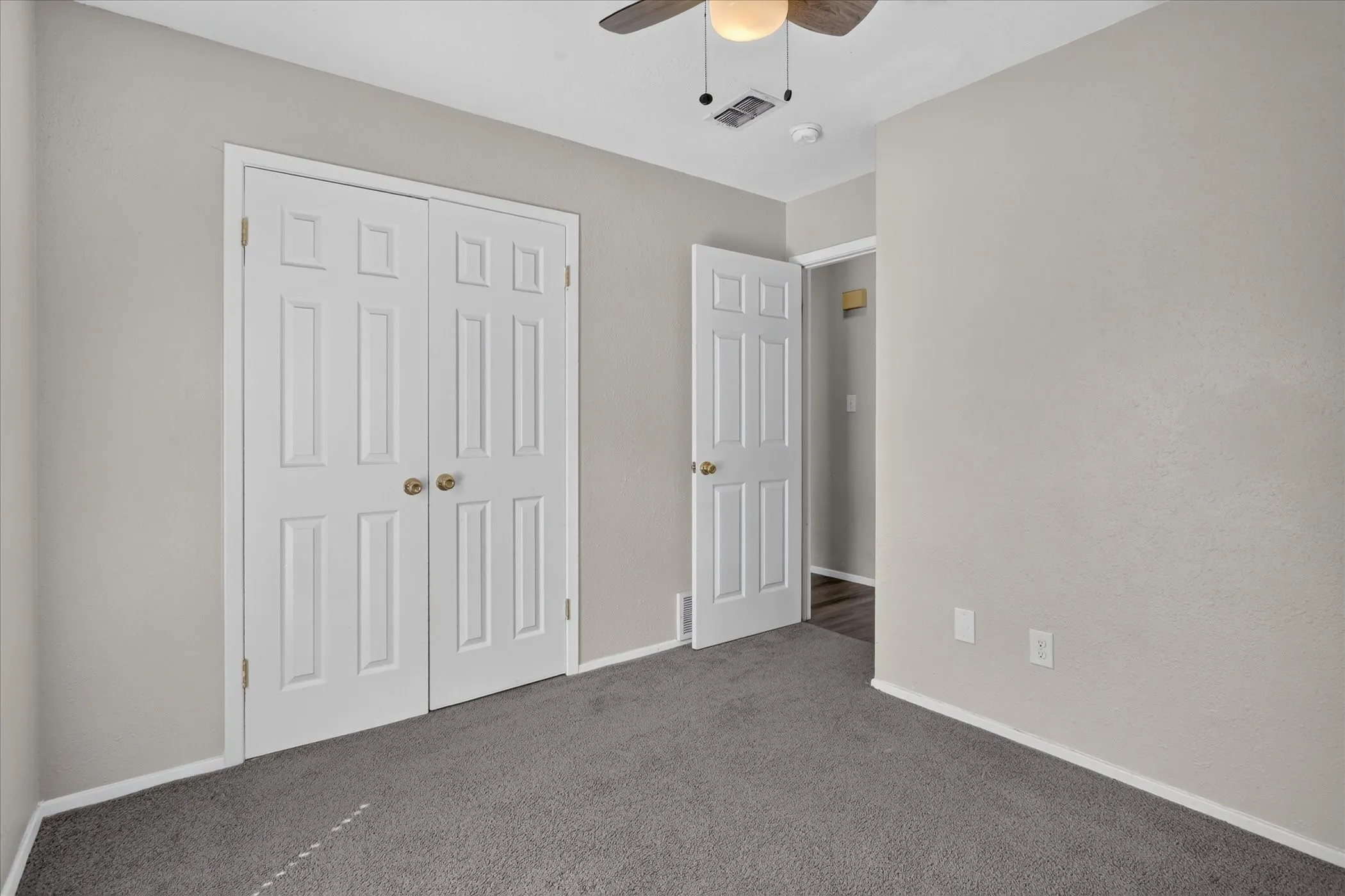 Neutral wall paint, textured carpeting, panel doors, and a ceiling fan with integrated lighting
