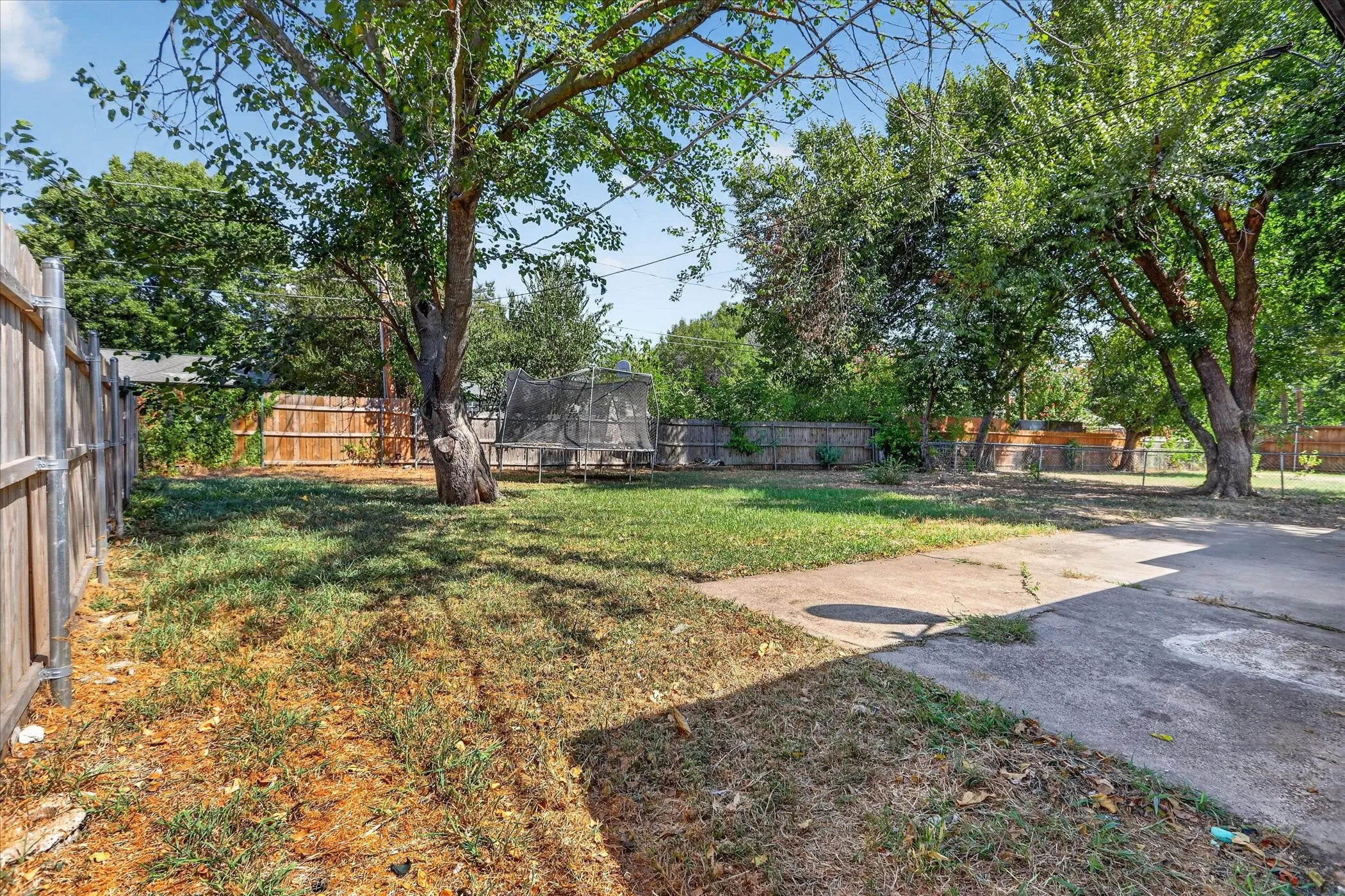 Expansive backyard featuring mature trees, partial wood fencing, and a concrete patio