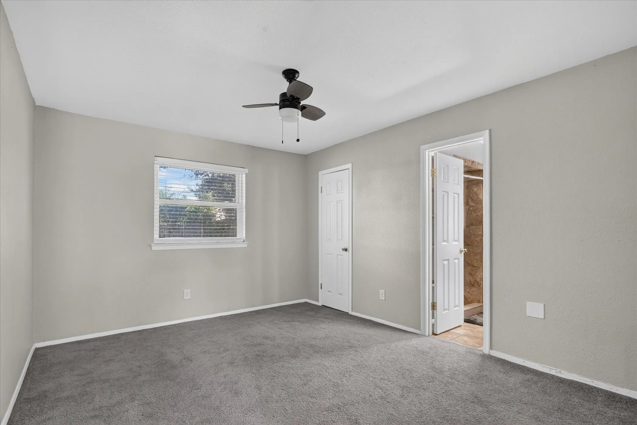 Neutral gray walls, dark gray carpeting, and a ceiling fan with integrated lighting