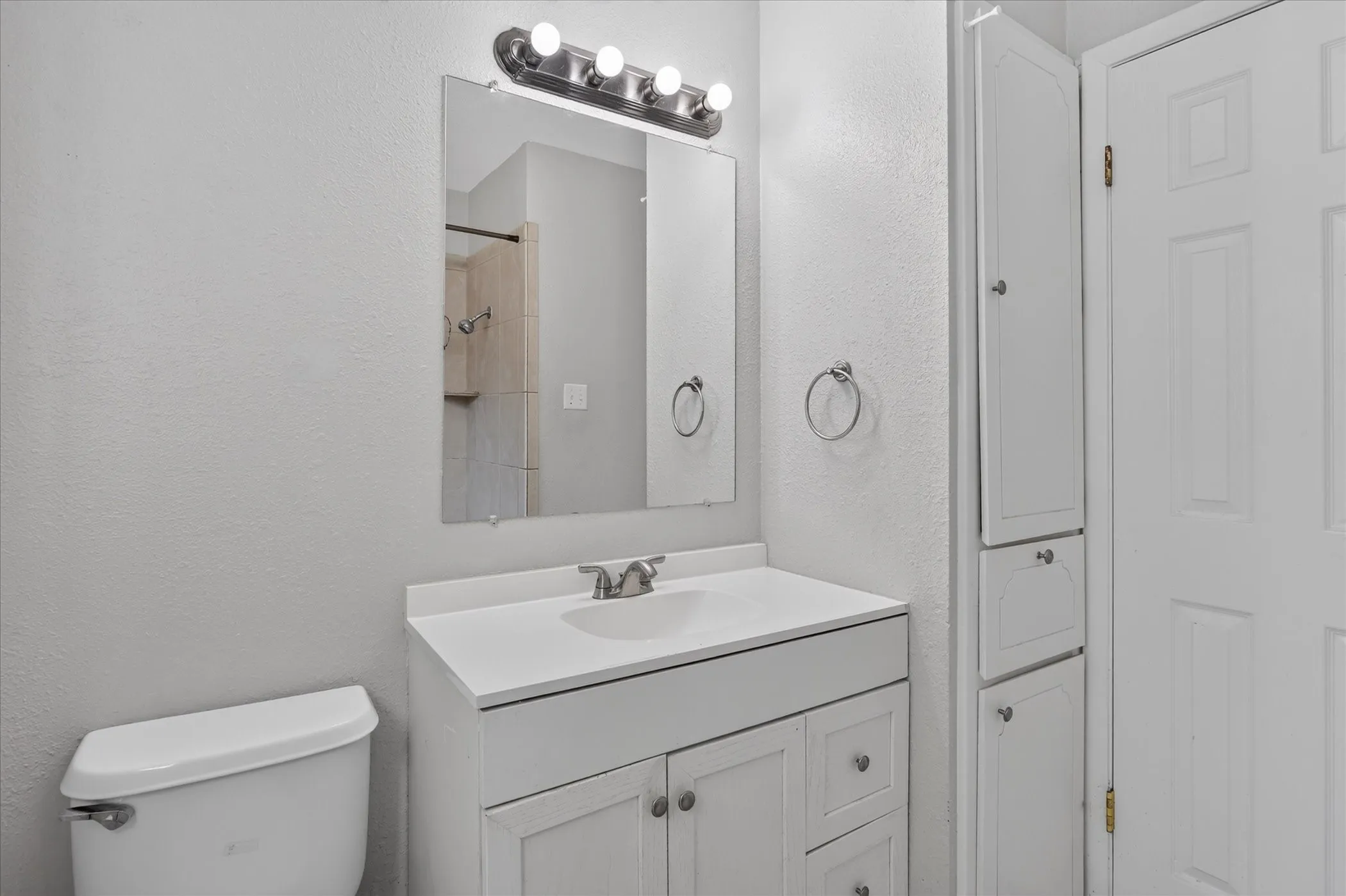 Neutral wall paint, vanity with integrated sink, chrome-finish faucet, wall-mounted mirror, and tiled shower surround