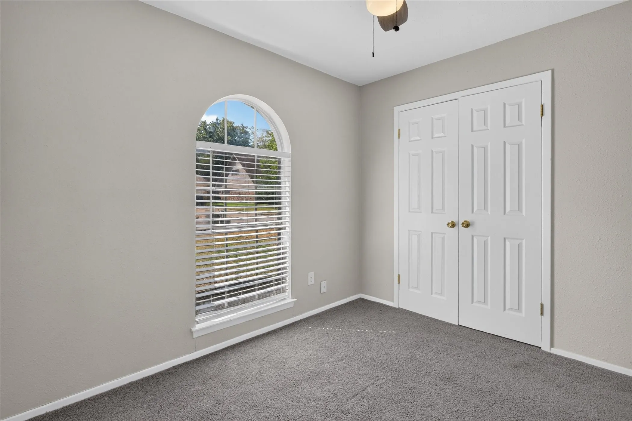 Arched window with blinds, bi-fold closet doors, ceiling-mounted light fixture, and carpeted flooring