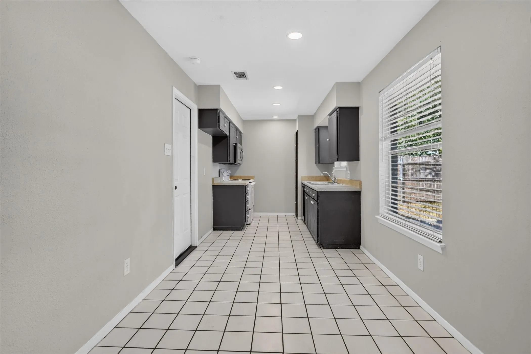 Kitchen featuring dark cabinetry, laminate countertops, a stainless steel microwave, a white electric range, and tiled flooring