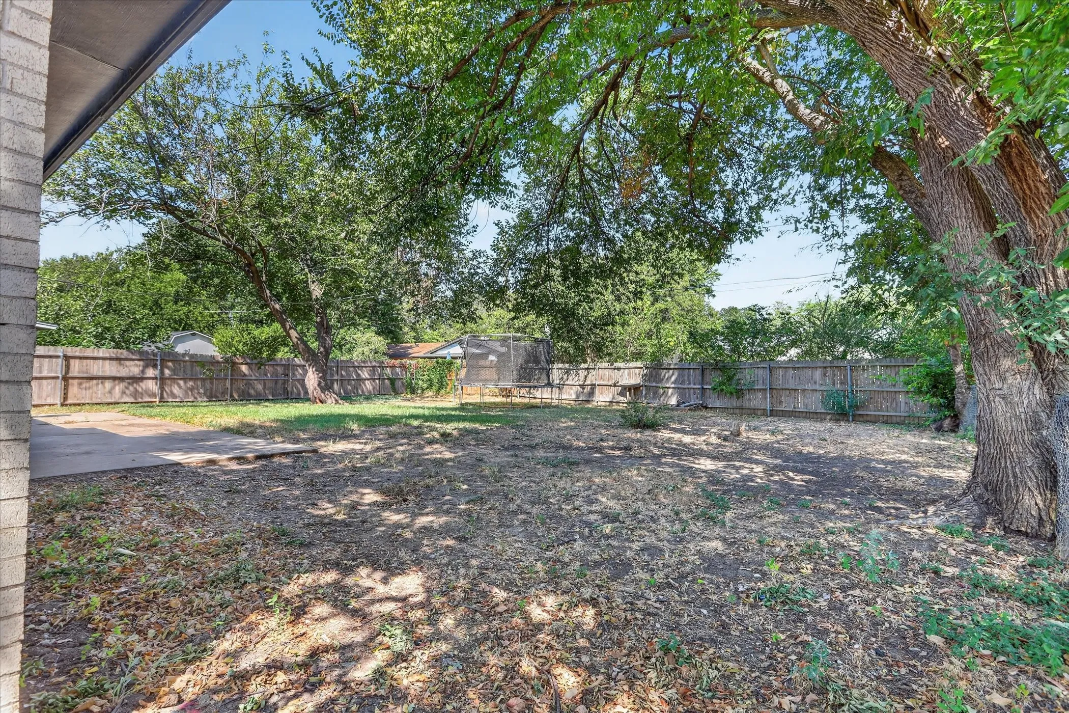 Expansive fenced yard with mature trees and a concrete patio