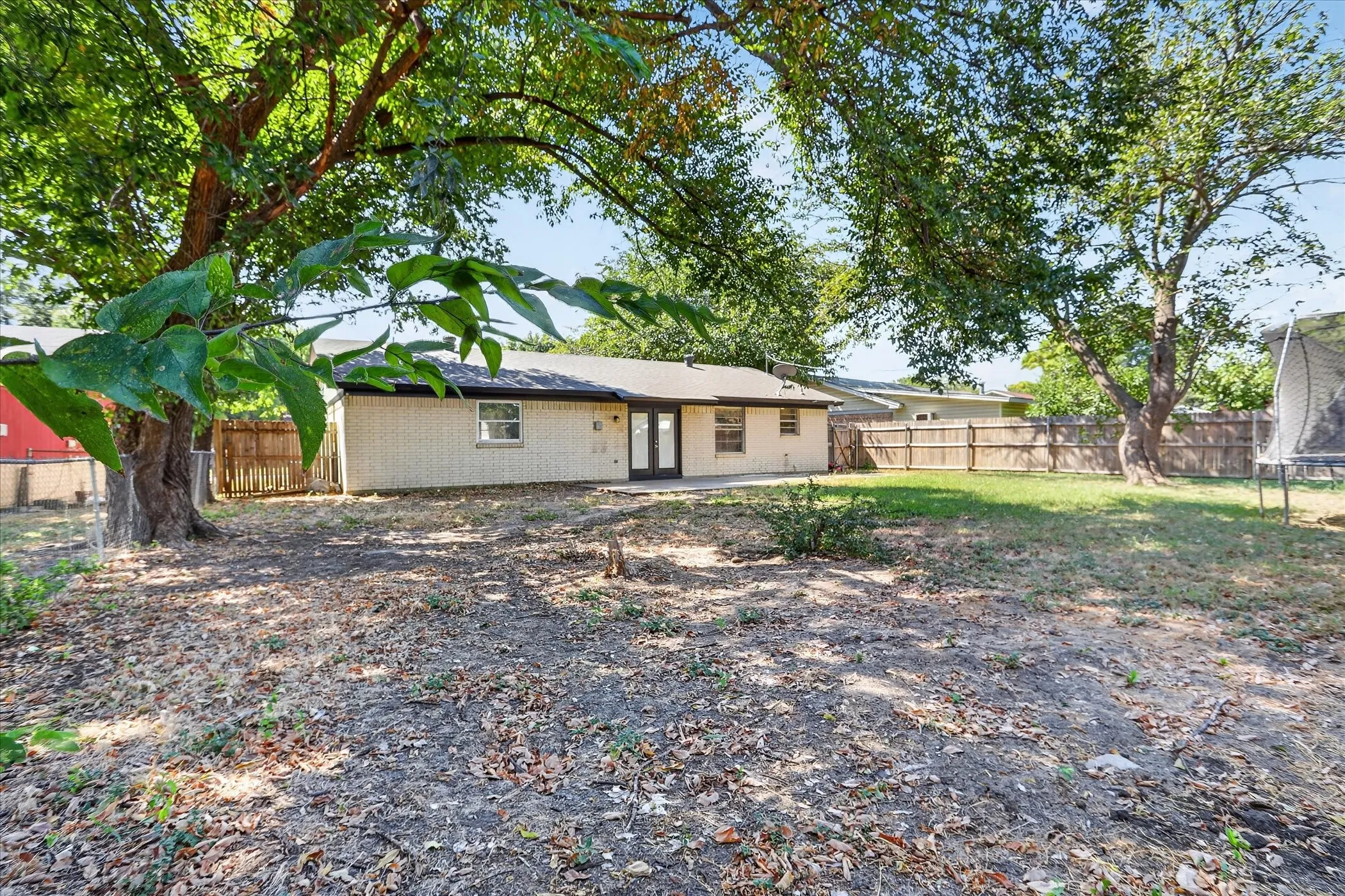 Expansive backyard featuring mature trees, a privacy fence, and an outdoor patio area
