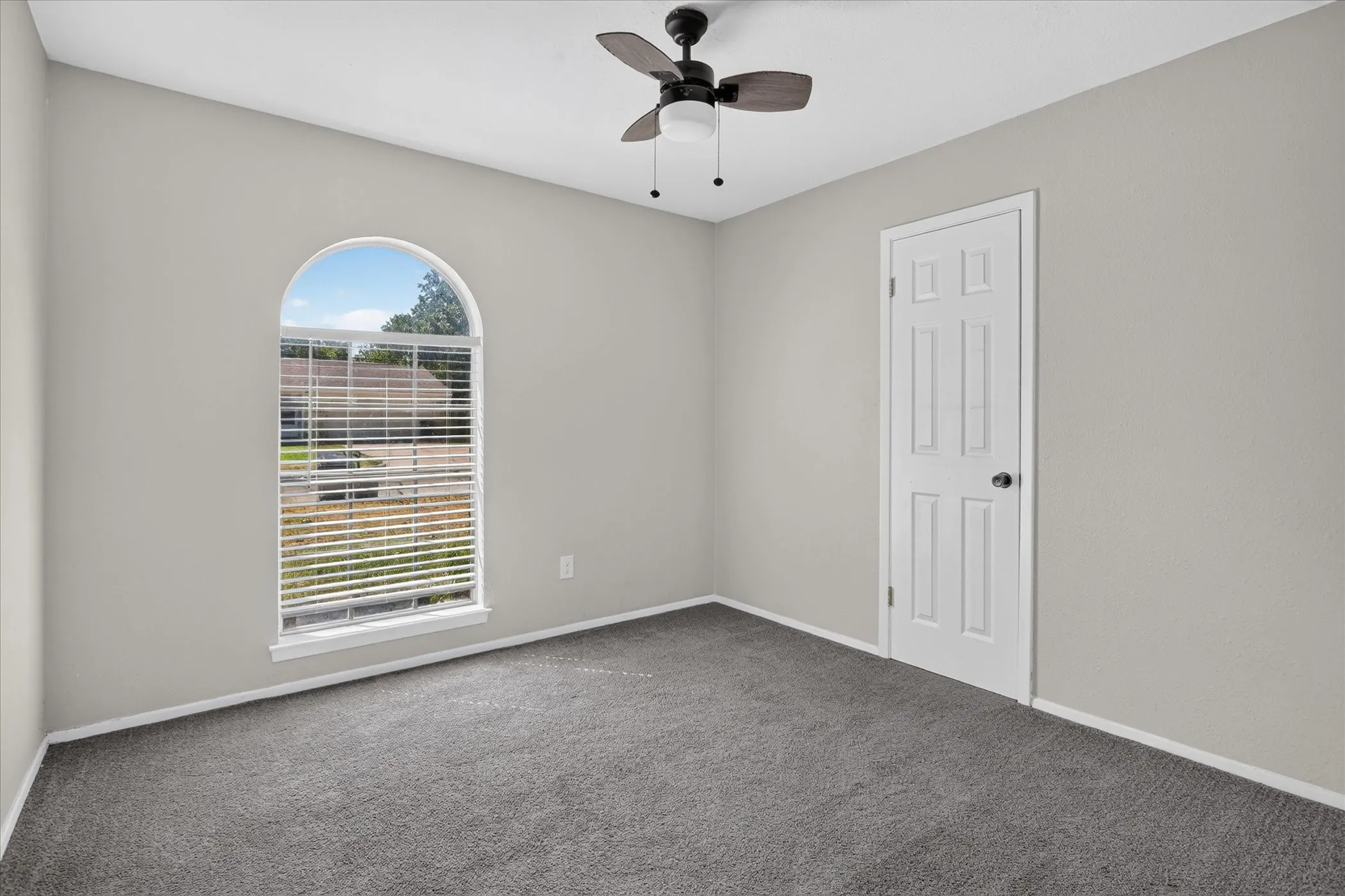 Arched window with blinds, ceiling fan, six-panel door, and gray carpet flooring