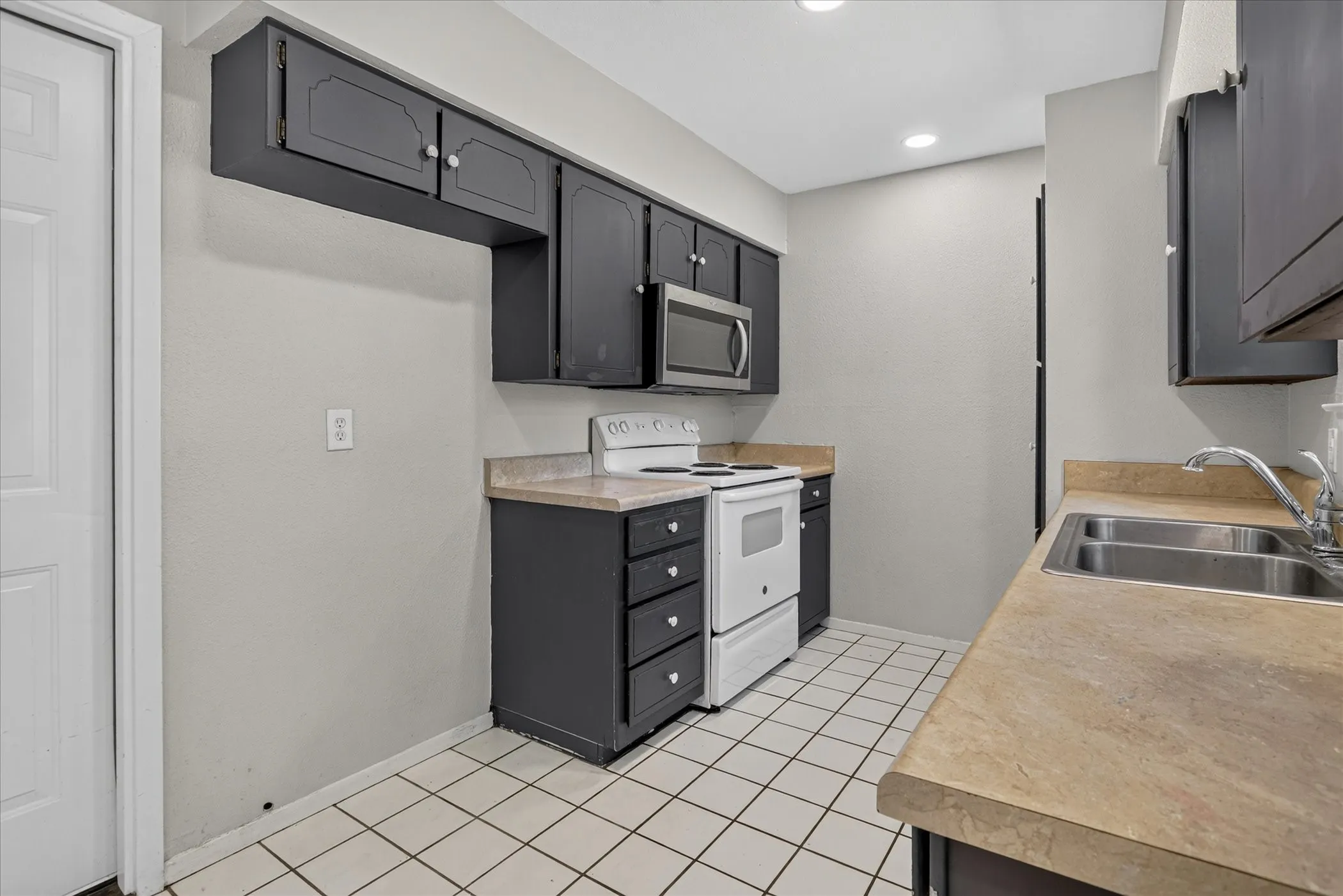 Tile flooring, dark cabinetry, built-in microwave, and recessed lighting