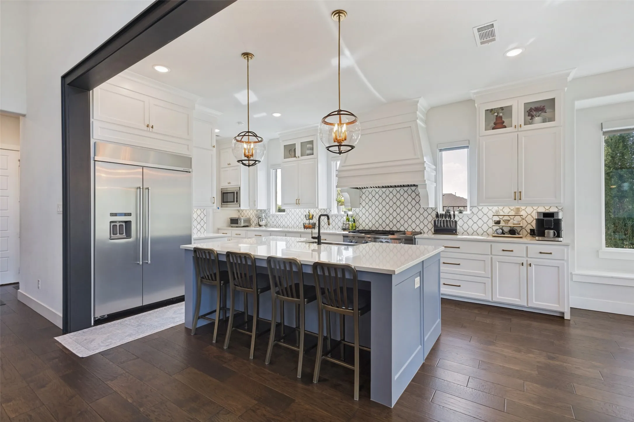 Kitchen featuring wood-finish flooring, white cabinetry, integrated stainless steel refrigerator, kitchen island with seating, and decorative pendant lighting