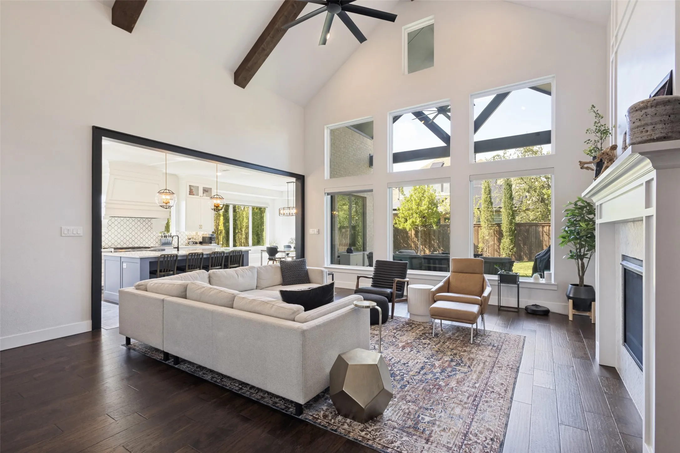 Vaulted ceiling with exposed wood beams, expansive floor-to-ceiling windows, dark wood-finish flooring, and a built-in fireplace with a white mantel
