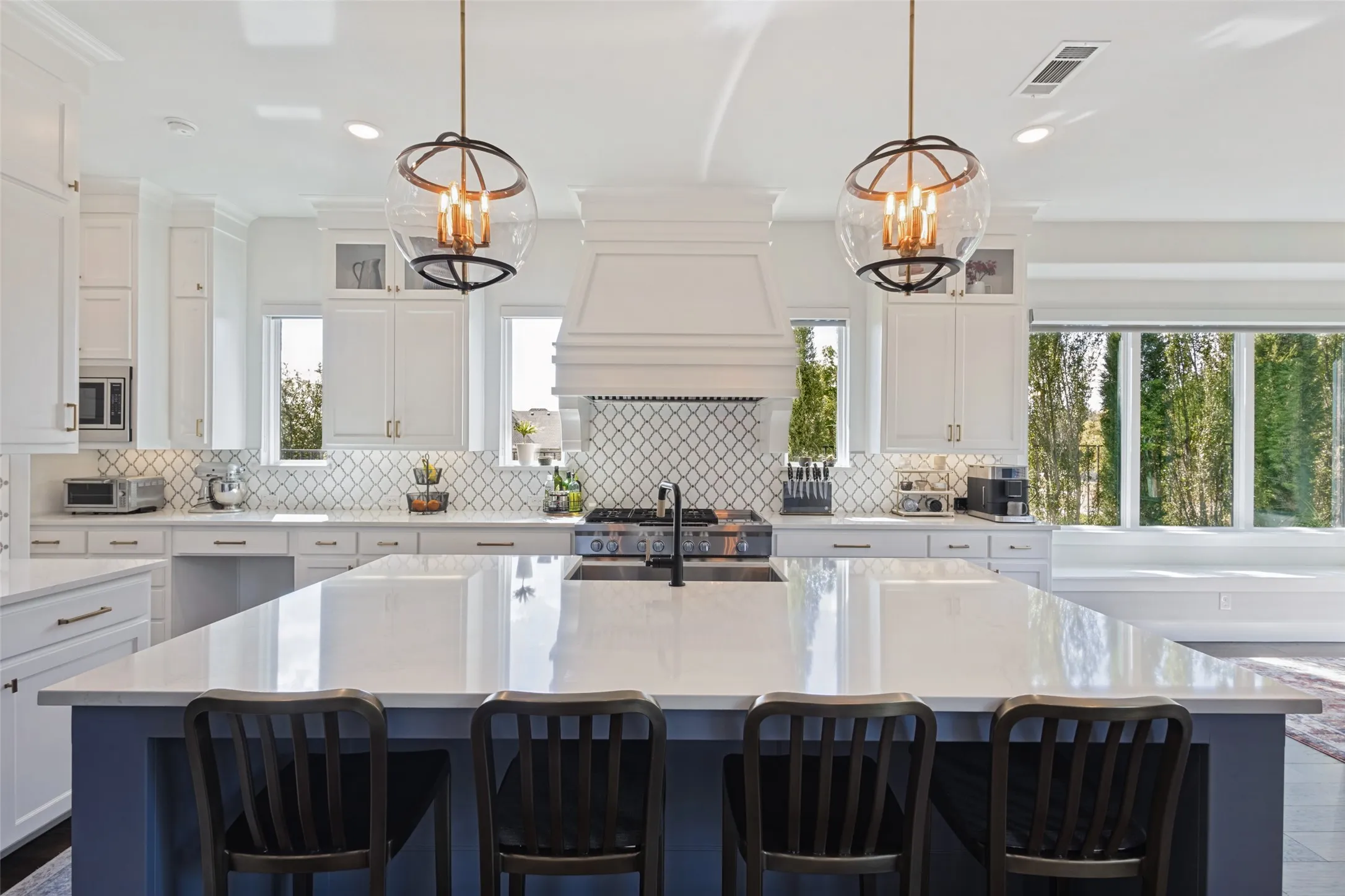 Spacious kitchen with a large island, white cabinetry, integrated range hood, patterned tile backsplash, and oversized windows