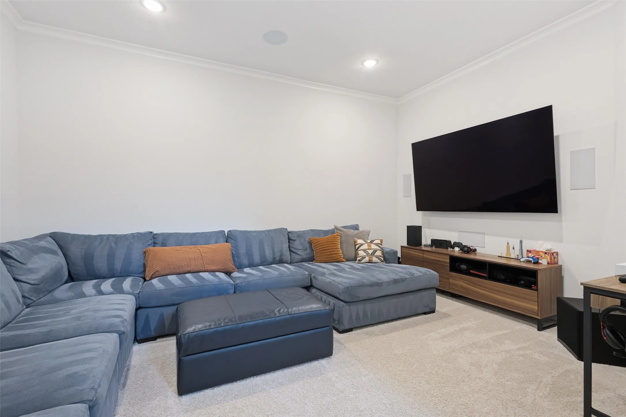 Recessed lighting, crown molding, wall-mounted television, and a wood-finish media console