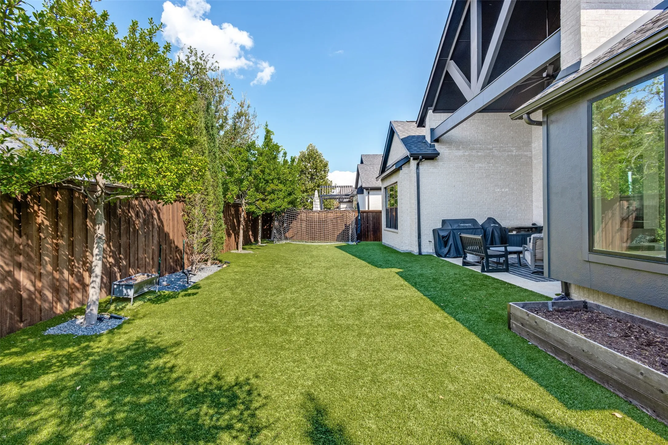 Expansive backyard featuring artificial turf, wood fence, mature trees, and a raised planter box