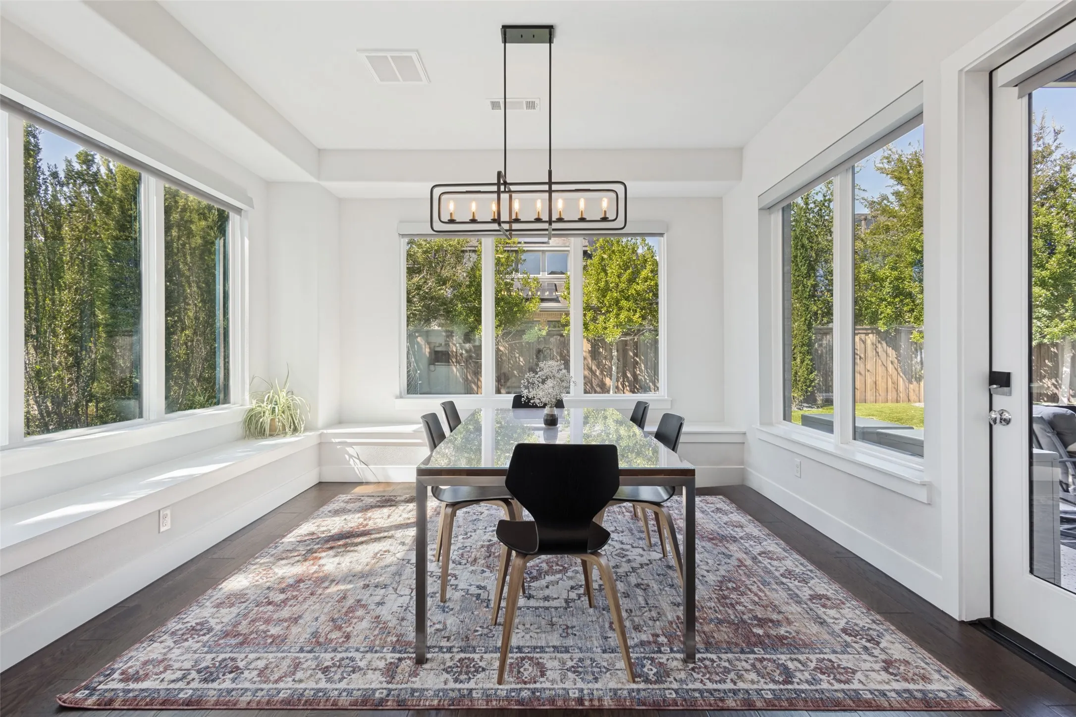 Window-lined dining area with dark wood-finish flooring, a contemporary chandelier, and a built-in window bench