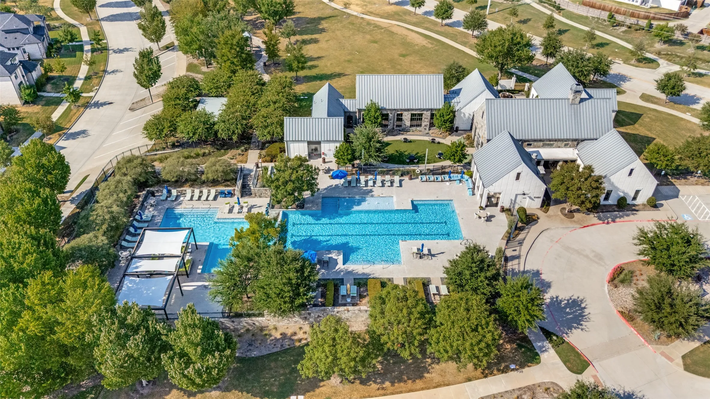 Expansive outdoor pool with multiple lounging areas, shaded pergolas, and adjacent recreational building with stone and siding exterior