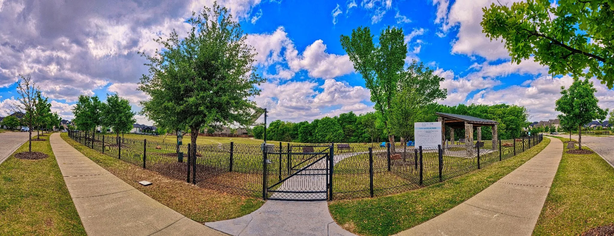 Fenced community green space featuring a covered pavilion, walking paths, and mature trees