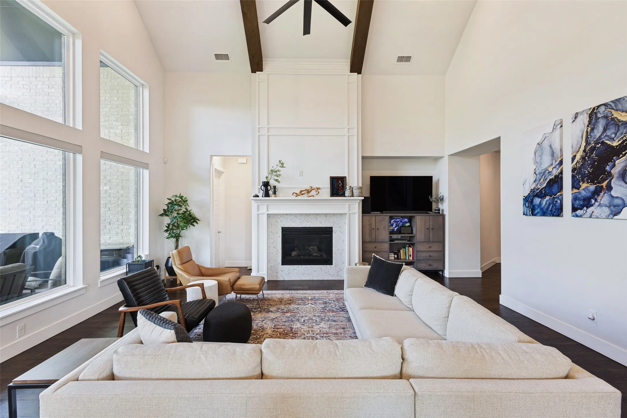 Vaulted ceiling with exposed wood beams, large windows, fireplace with tile surround, and dark wood-finish flooring