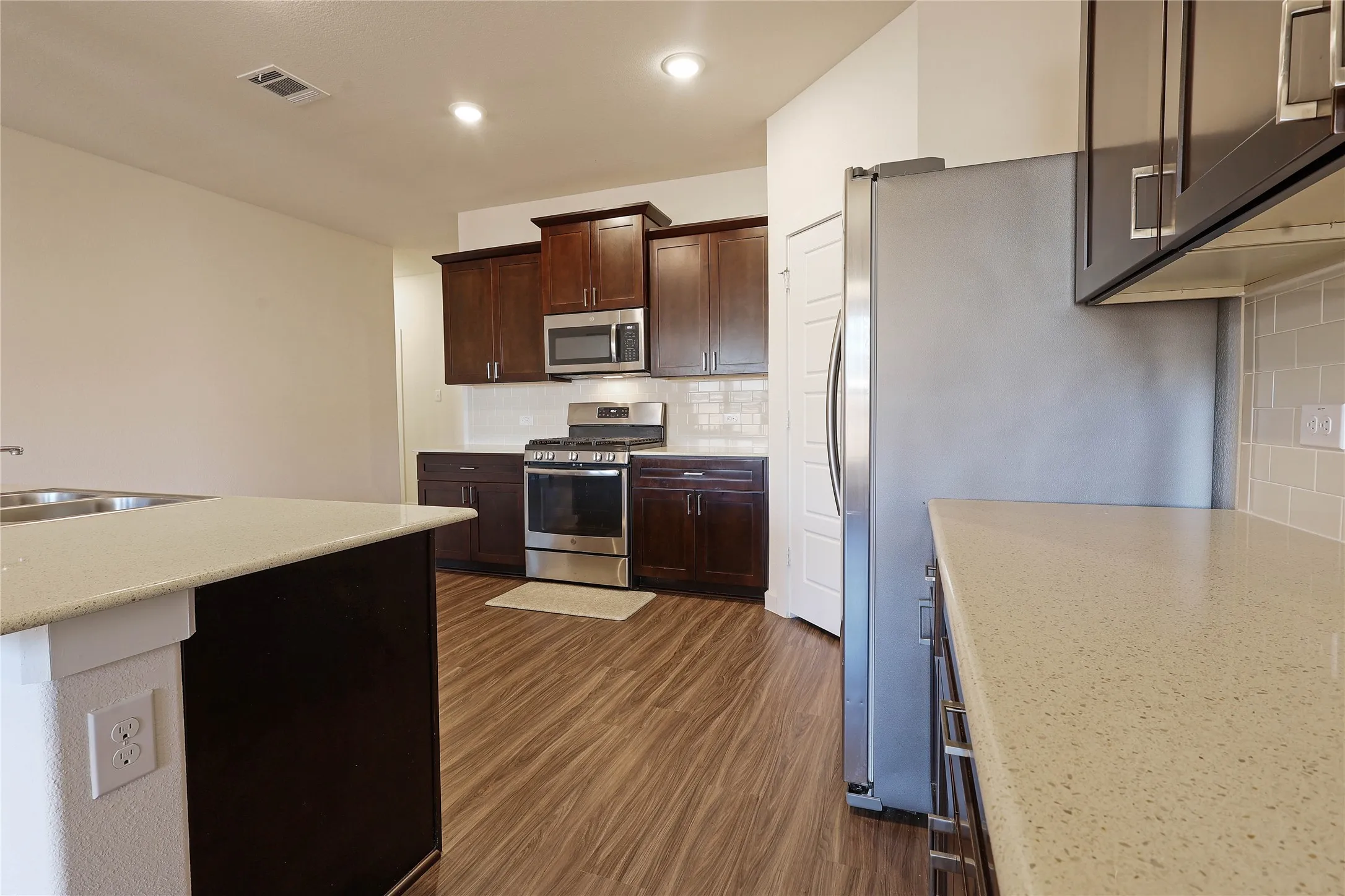 Kitchen featuring stainless steel appliances, dark wood cabinetry, light-toned countertops, tile backsplash, and wood-finish flooring