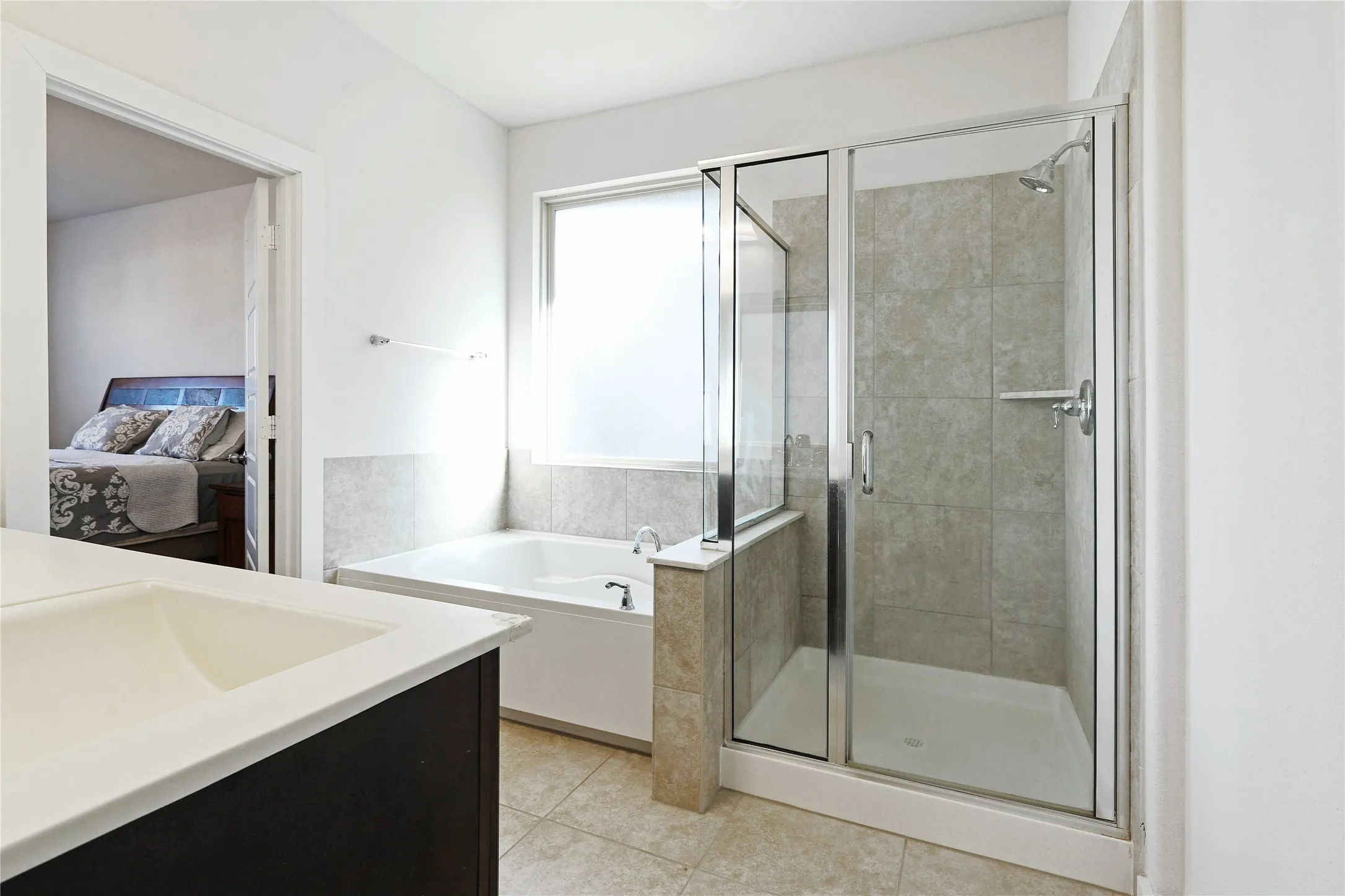 Built-in soaking tub with a large privacy window, walk-in shower with clear glass enclosure, and a vanity with an integrated sink