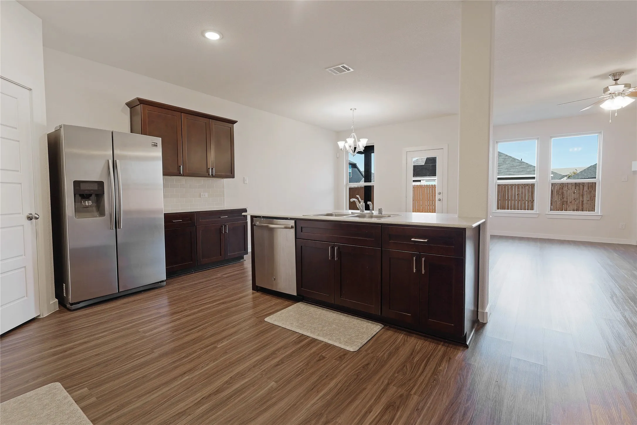 Open-concept kitchen with wood-finish flooring, dark wood cabinetry, stainless steel appliances, and a kitchen island with sink