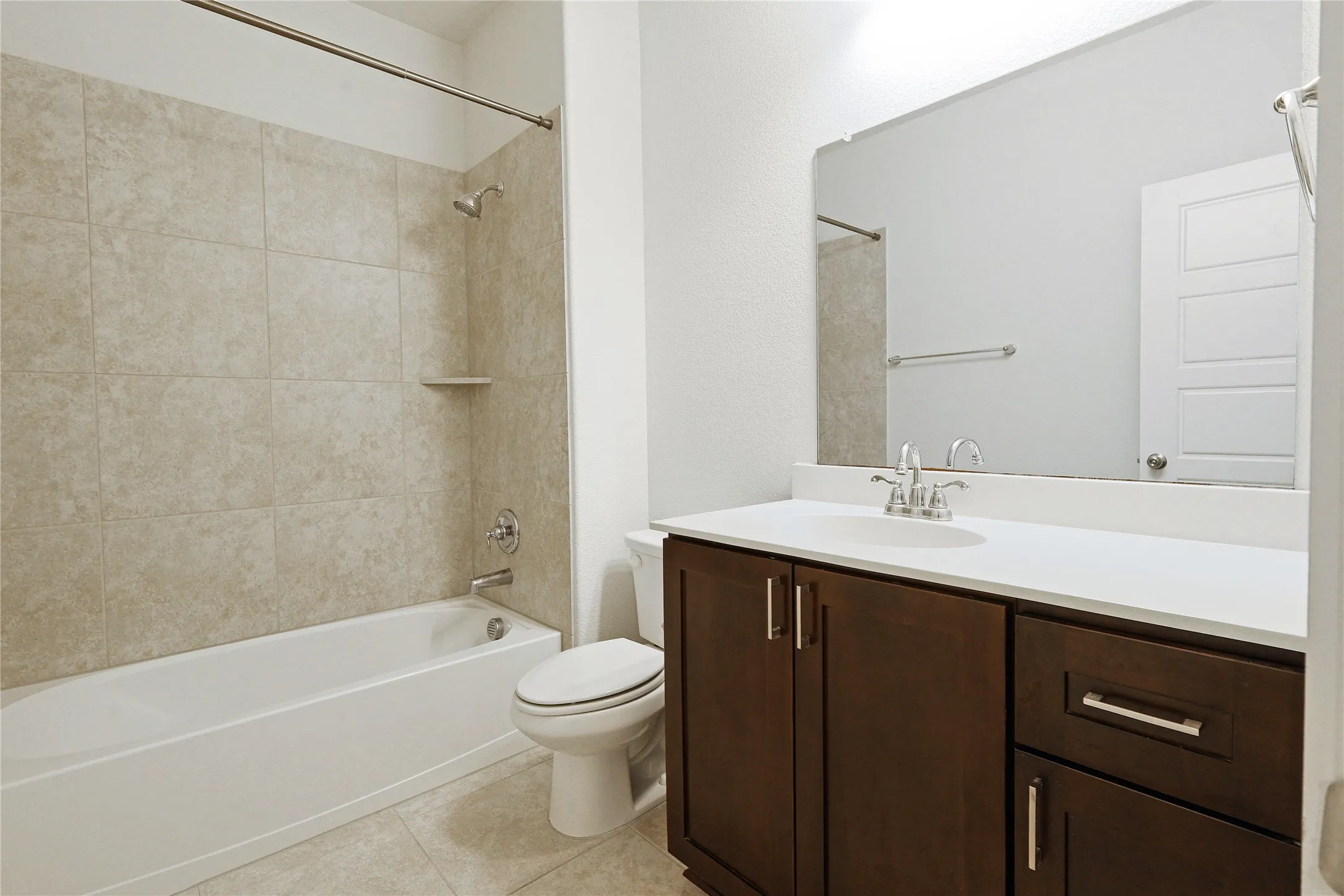 Bathroom featuring a bathtub with tiled surround, a built-in shower shelf, a vanity with dark wood-finish cabinetry, a white countertop, and a large wall-mounted mirror