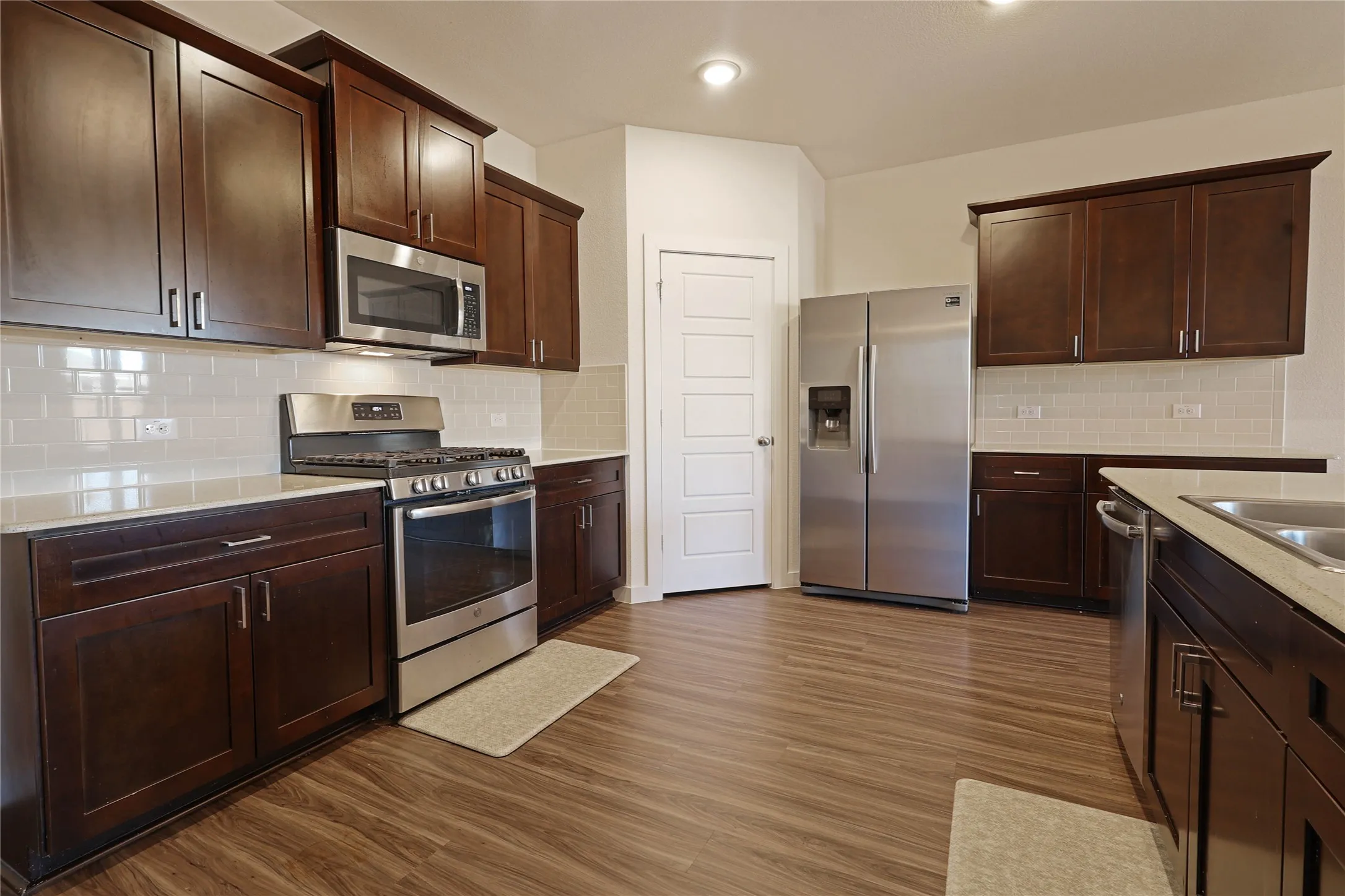 Kitchen featuring wood-finish flooring, dark wood cabinetry, stainless steel appliances, light-toned countertops, and a white subway tile backsplash