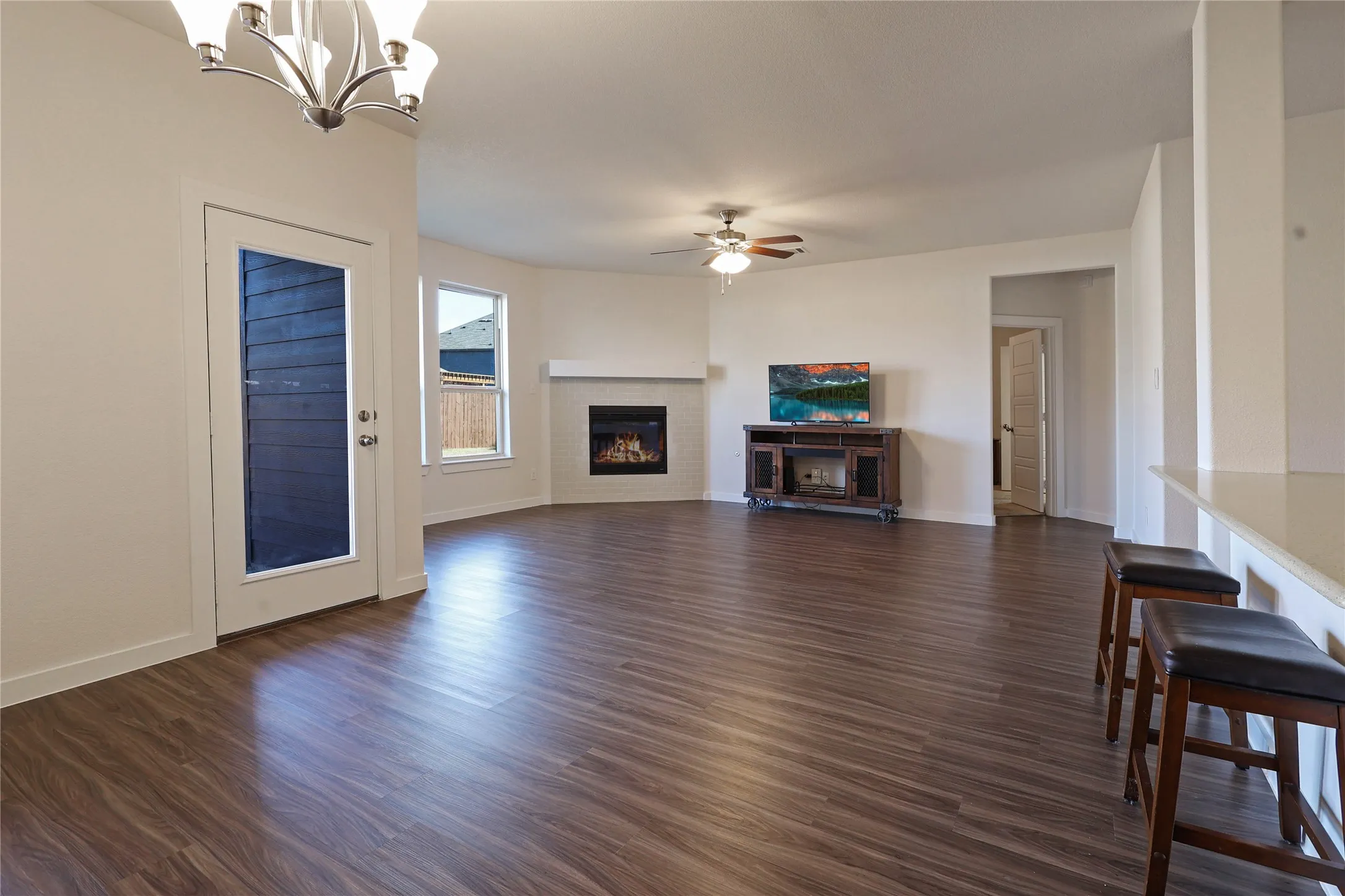 Open-concept living space featuring wood-finish flooring, a contemporary ceiling fan, and a gas fireplace with a white brick surround