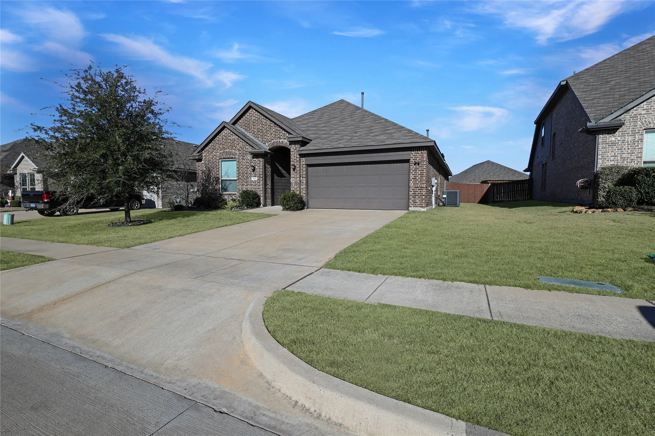 Brick exterior, attached garage, concrete driveway, front yard landscaping, mature tree